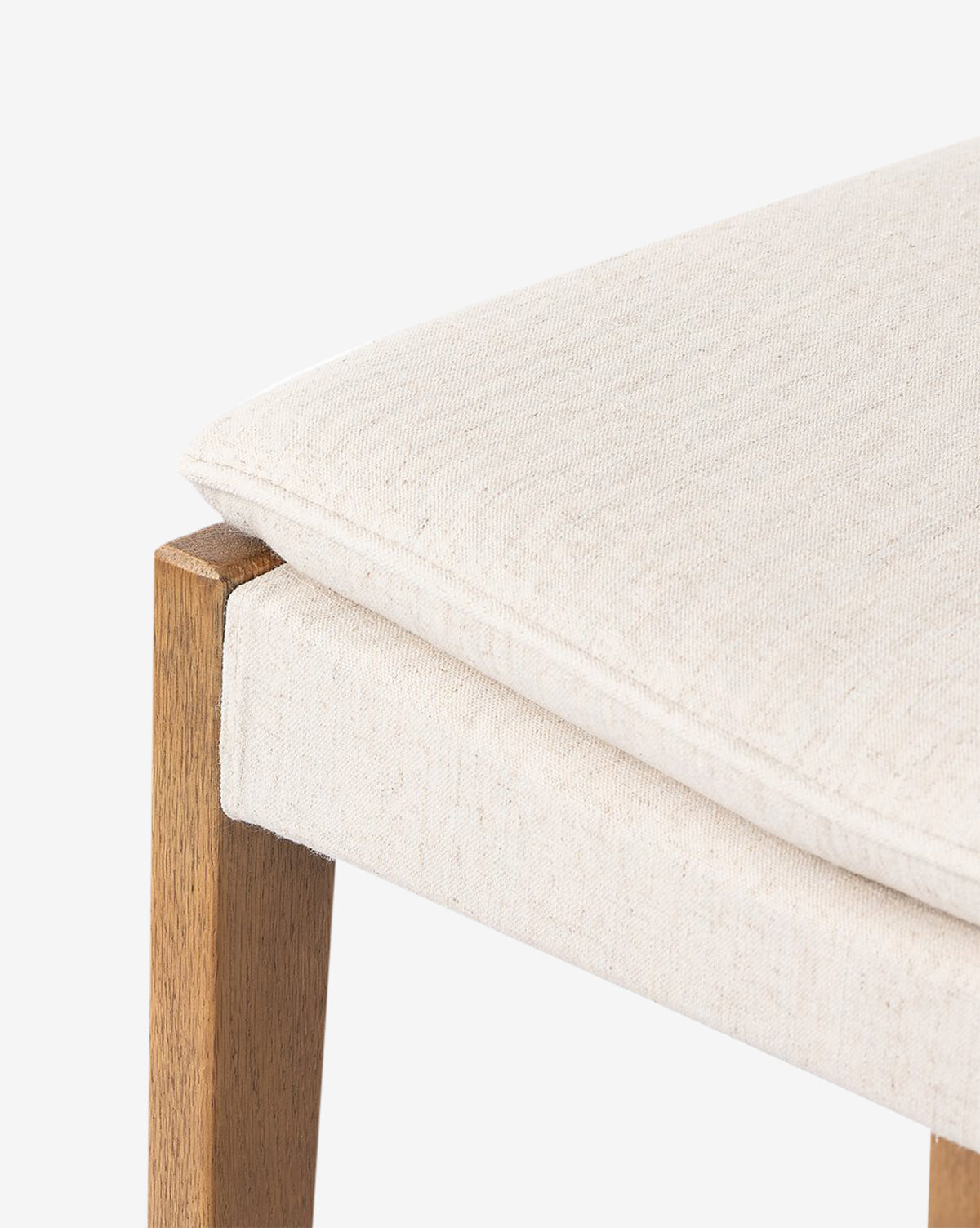 Close-up of the Four Hands Kaelith Counter Stool, showcasing its light beige upholstered seat and solid oak legs against a plain white background. Vendixs