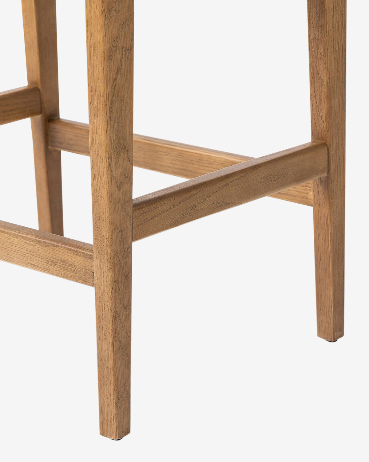 Close-up of the lower legs and footrest of the Four Hands Kaelith Counter Stool, highlighting its natural wood grain and light brown solid oak finish against a white background. Vendixs