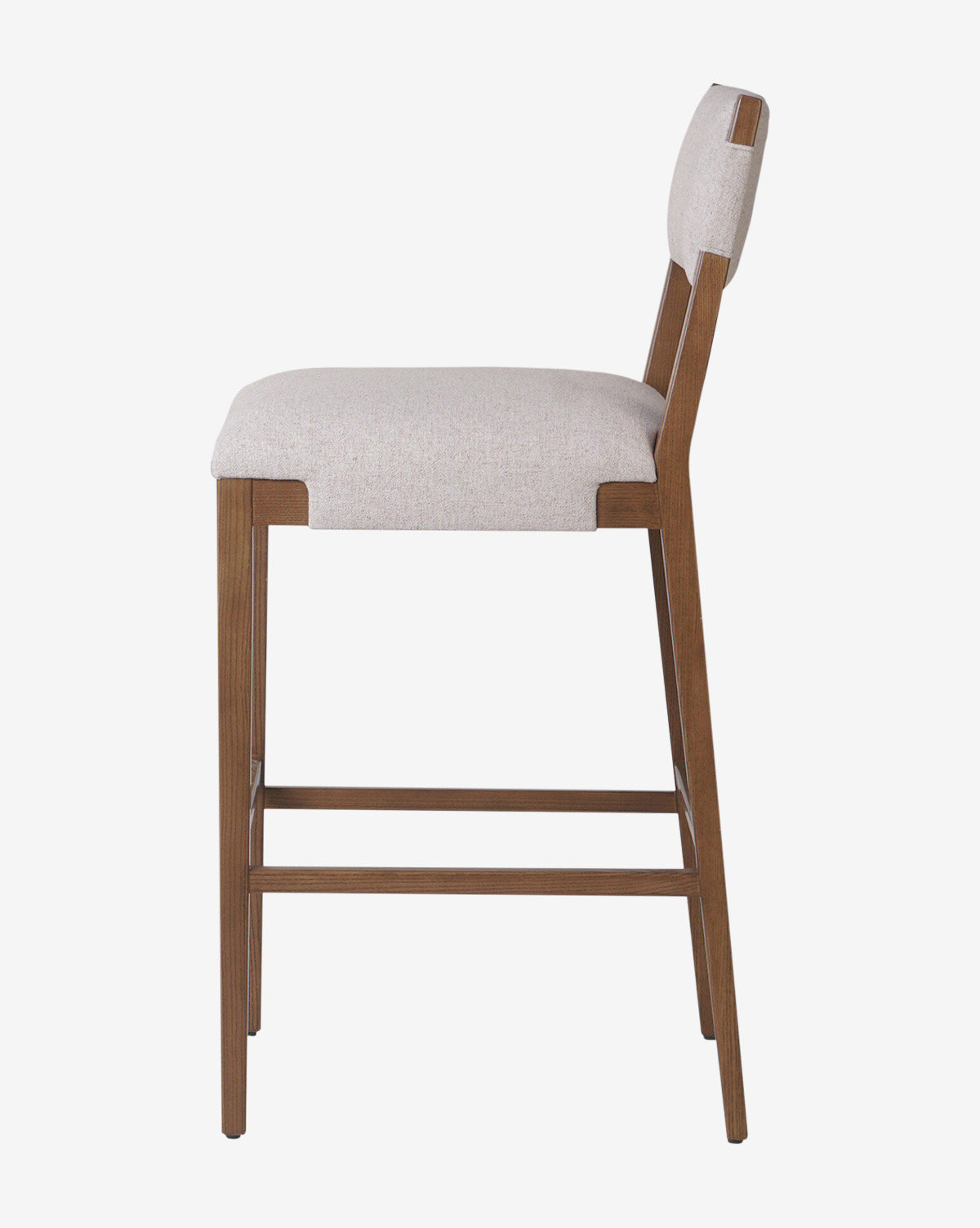The Kennebec Stool by Four Hands features a side view of a modern design with a light beige performance fabric-upholstered seat and backrest, supported by an ash wood frame and legs with horizontal support bars by Vendixs