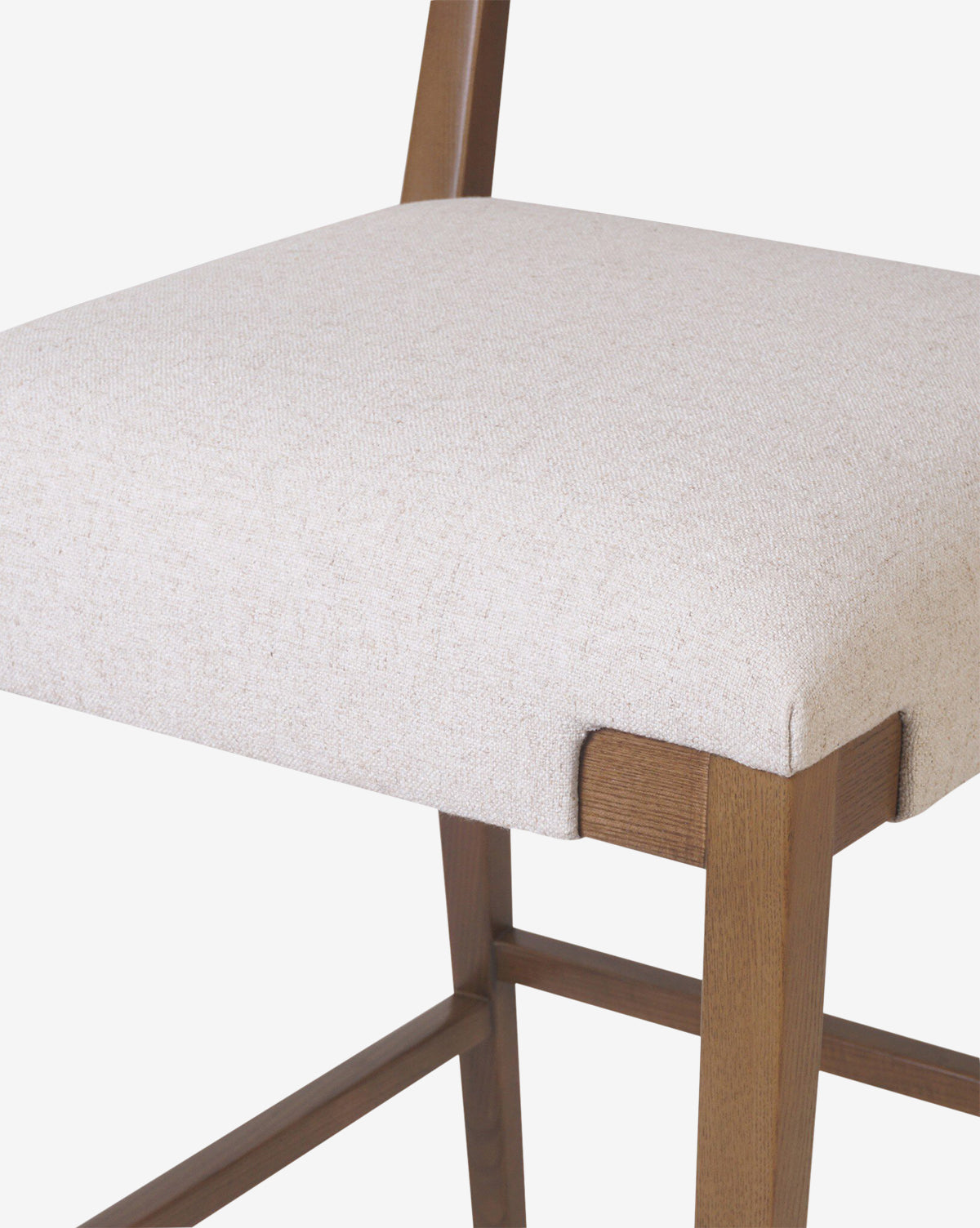 Close-up of the Four Hands Kennebec Stool, featuring a light beige performance fabric cushioned seat and ash wood frame, highlighting part of the backrest and legs against a plain white background. Vendixs
