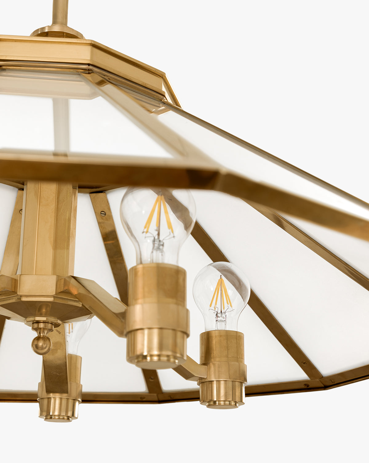 Close-up of the Knightley Chandelier in antique brass, featuring three exposed LED filament bulbs and a geometric glass shade against a light background, by Vendixs