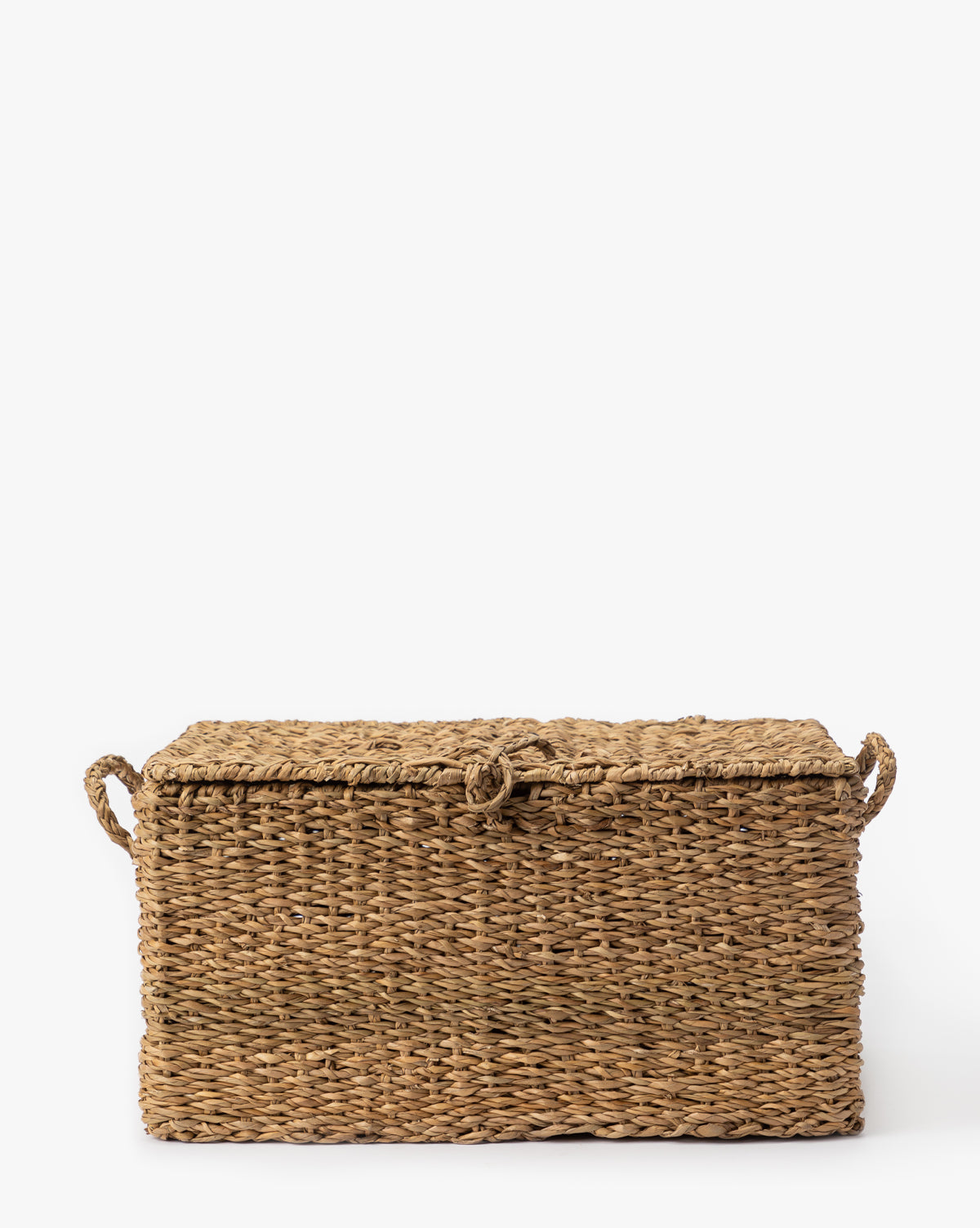 The Kya Seagrass Box is a rectangular, hand-woven storage box with a lid and side handles, crafted from natural light brown seagrass fibers and shown against a plain white background by McGee & Co.