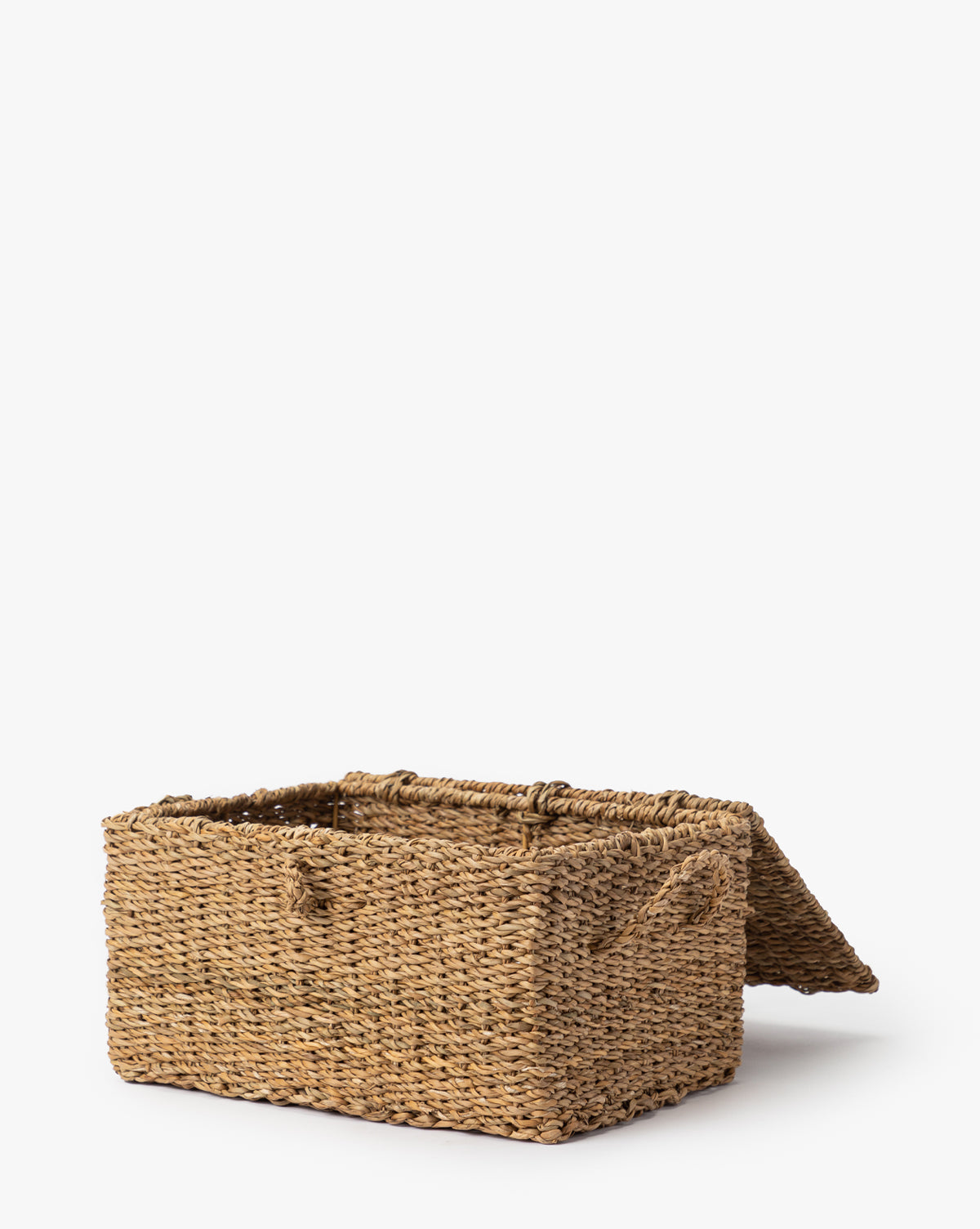 The Kya Seagrass Box, a rectangular hand-woven basket with a hinged lid made from natural fibers, is shown partially open on a plain white background by Vendixs