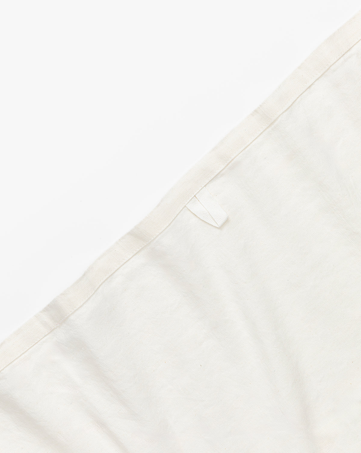 A close-up of an off-white cotton-linen blend fabric with a stitched edge and small white loop, set against a white background—ideal as stylish Lace Tea Towels (Set of 2) for your kitchen, by Vendixs