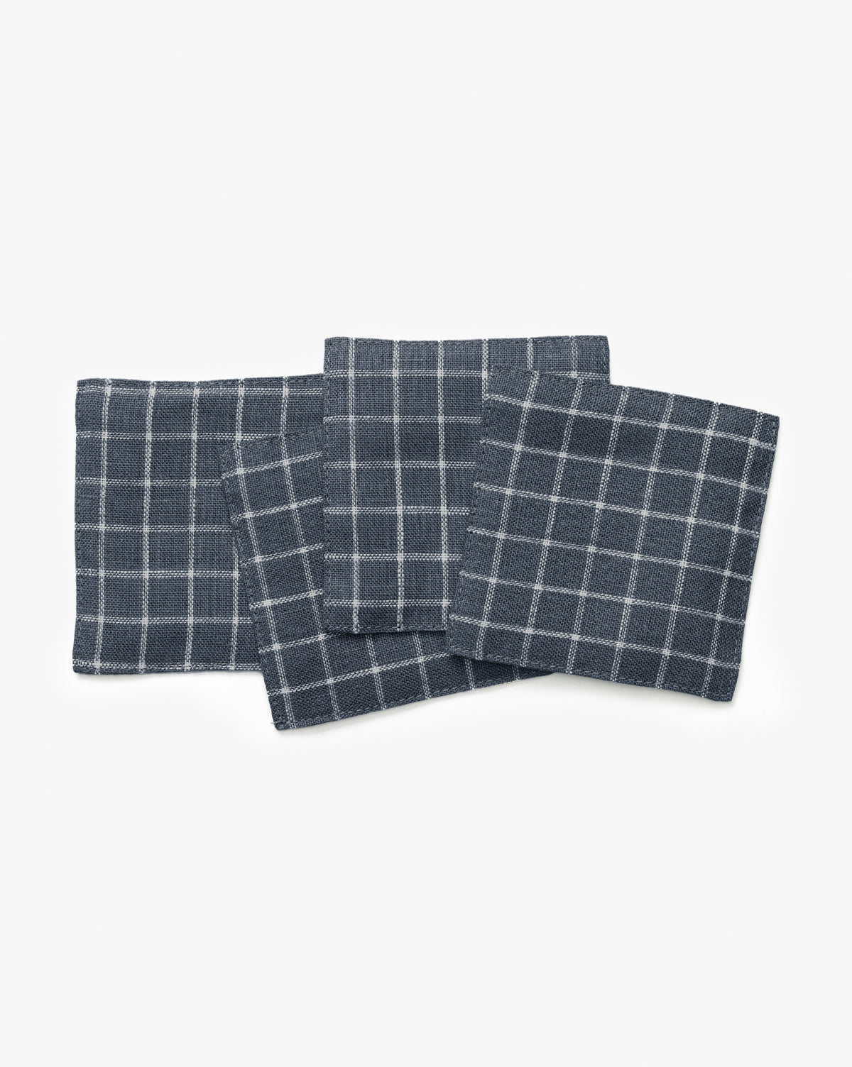 The Lancaster Linen Coaster Set (Set of 4) features dark gray linen coasters with a white grid pattern, arranged with slight overlap on a white background for a stylish and absorbent table solution, by Vendixs