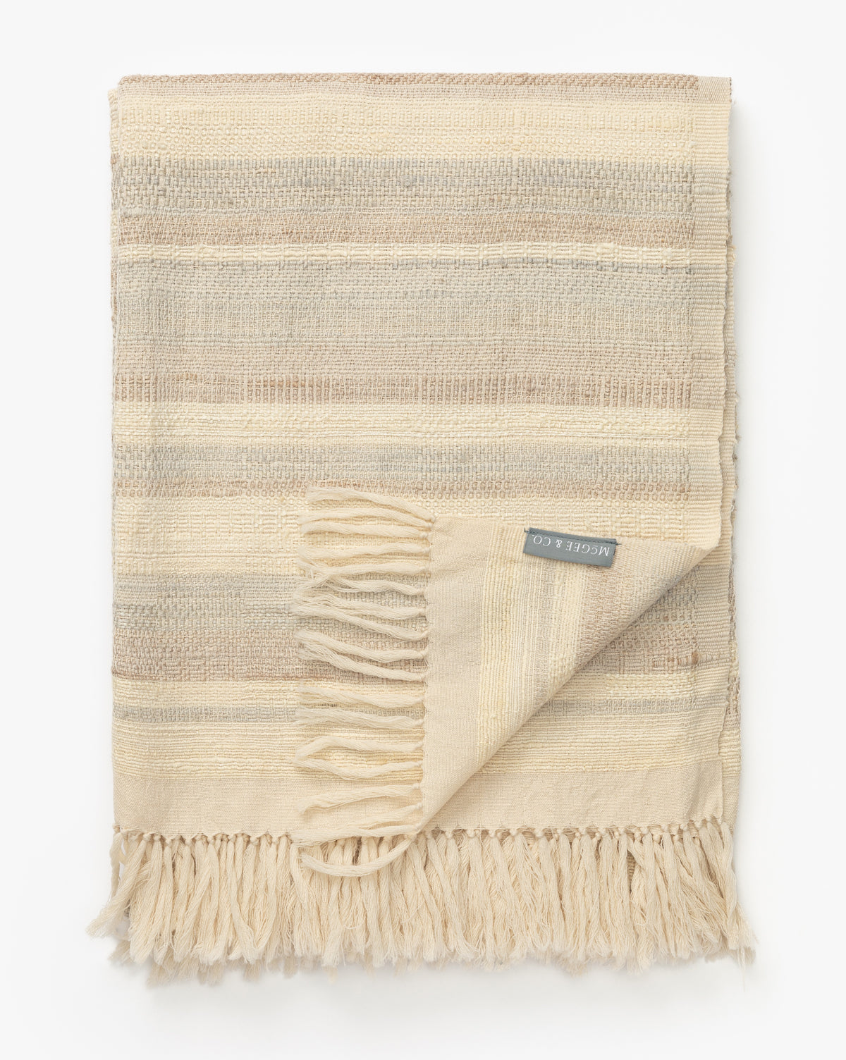 The Laney Stripe Throw by TAL HANDWOVEN CLASSICS LLP features beige and cream woven stripes, fringed edges, and a fabric label—luxuriously displayed on a white background, perfect for elevating any space. Vendixs