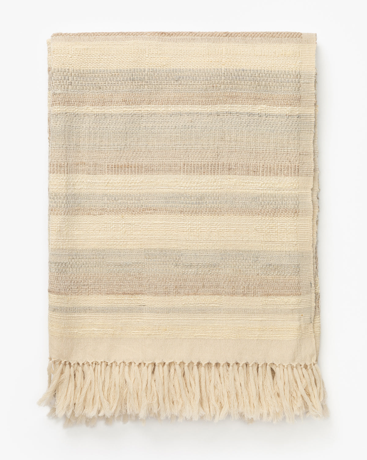 The Laney Stripe Throw by TAL HANDWOVEN CLASSICS LLP is a folded wool and silk blanket with beige, cream, and light brown horizontal stripes and fringe tassels along the bottom edge, displayed on a white background, Vendixs