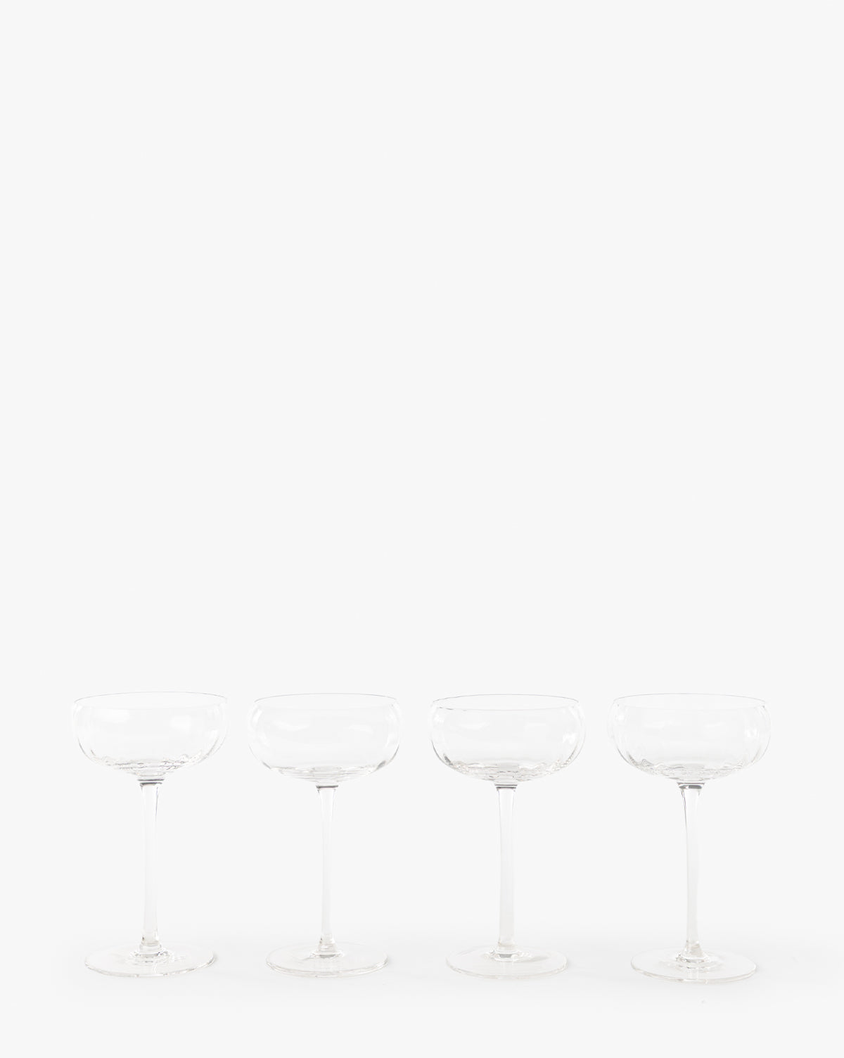 A set of four clear Langford Coupe glasses is evenly spaced in a row against a plain white background, highlighting this elegant glassware perfect for any celebration, by Vendixs