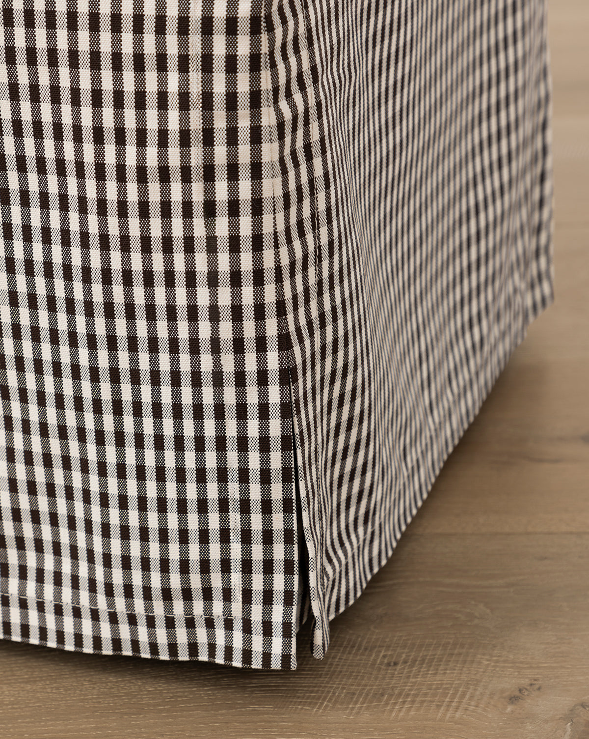 Close-up of the Makerspalm Latimer Ottoman (Ready to Ship), featuring black and white gingham check high-quality fabric, resting on a light wood floor. Vendixs