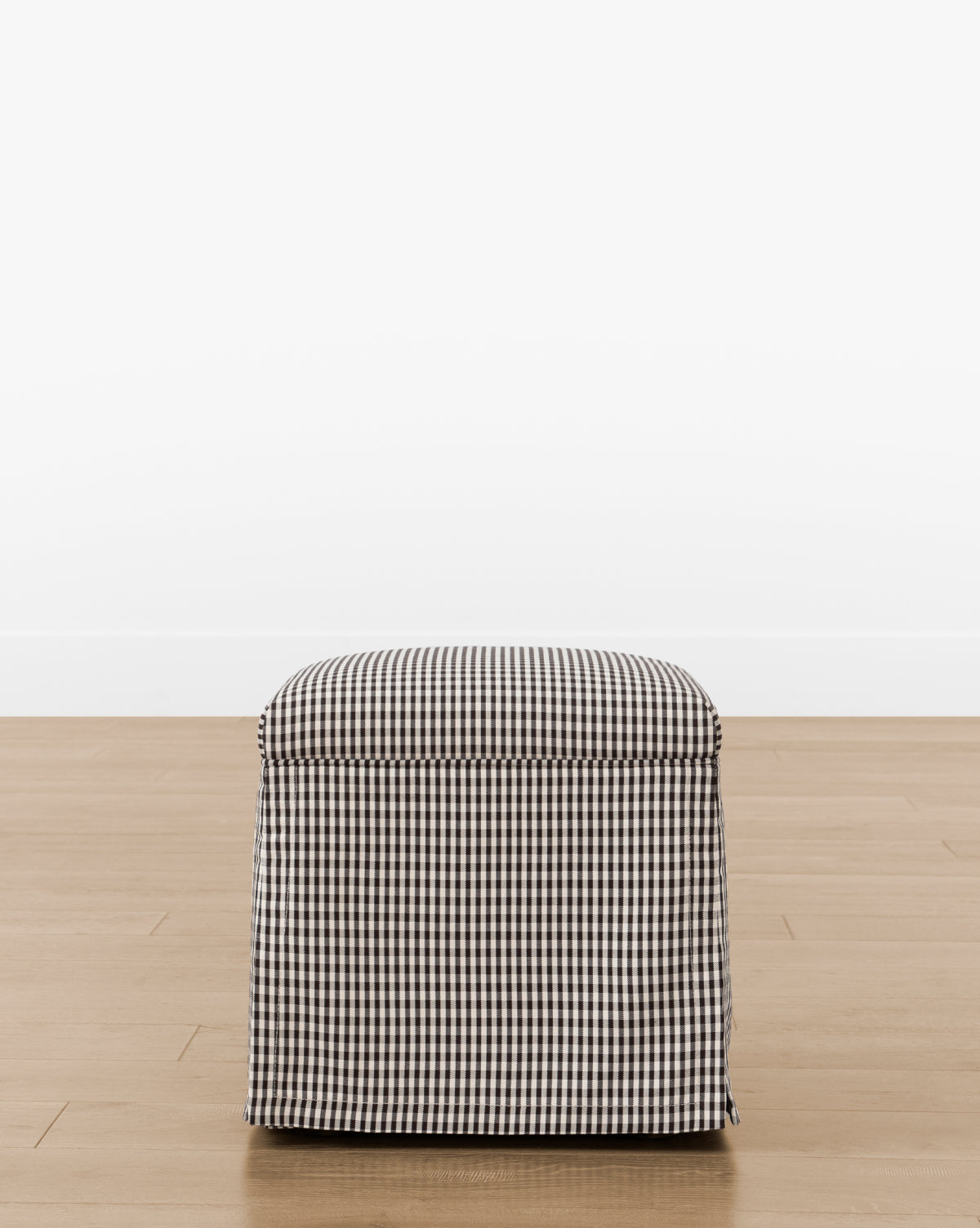 The Makerspalm Latimer Ottoman (Ready to Ship) features a compact square design in premium black and white gingham fabric, shown on a light wood floor with a plain white backdrop—a stylish and practical accent for any room. Vendixs