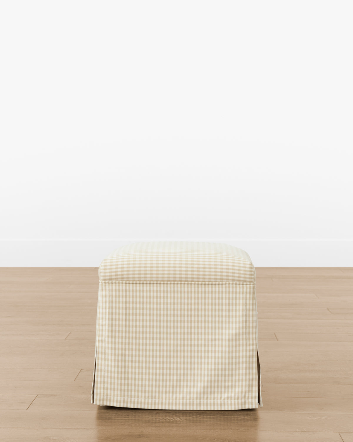 The Makerspalm Latimer Ottoman (Ready to Ship) features high-quality beige and white checkered fabric with a skirted cover, adding functional style to any room. Shown on a wooden floor against a white wall. Vendixs
