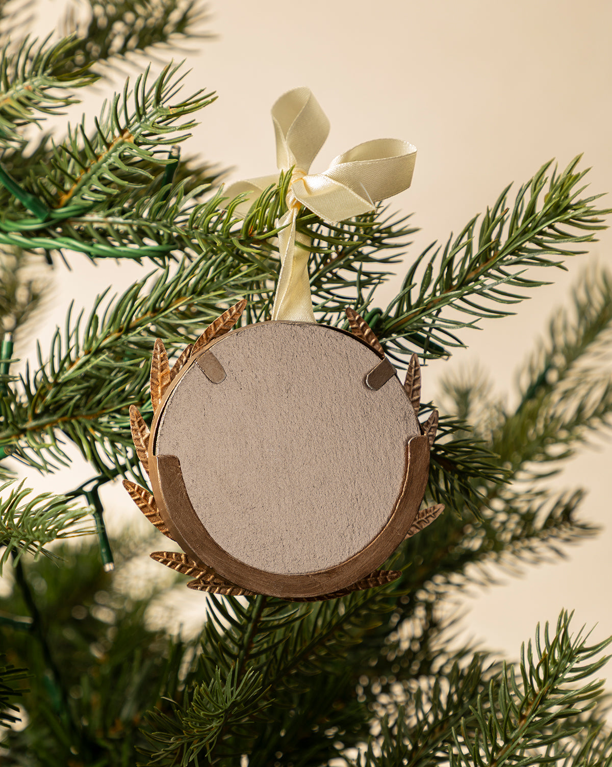 The Laurel Picture Frame Ornament is a round, blank wooden frame with a gold border and cream ribbon, hanging from a green Christmas tree—perfect as a holiday ornament or sentimental gift, by Vendixs