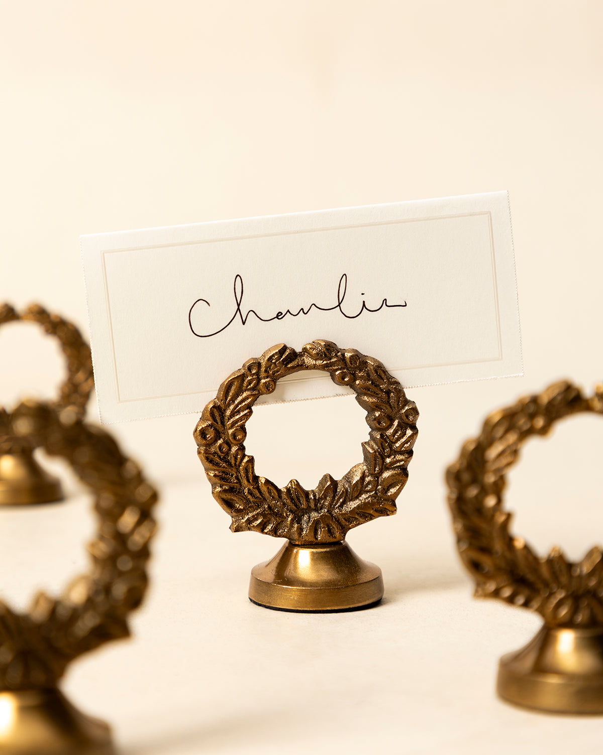 A white place card reading "Charlie" in cursive is displayed in a Laurel Place Card Holder (Set of 4), ideal for holiday tables, surrounded by matching holders on a cream background, by Vendixs