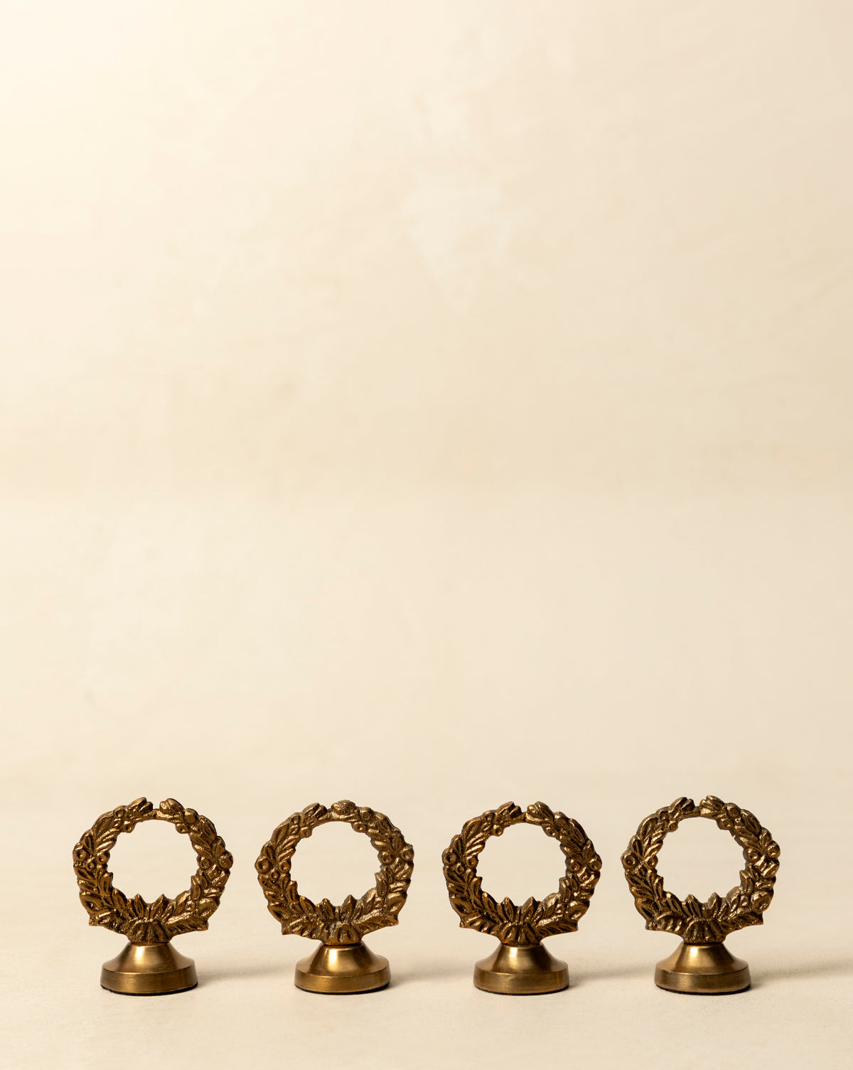 A set of four Laurel Place Card Holders, each shaped like a laurel wreath in gold, is arranged on a plain beige surface with a neutral background—perfect for adding elegance to your holiday table, by Vendixs