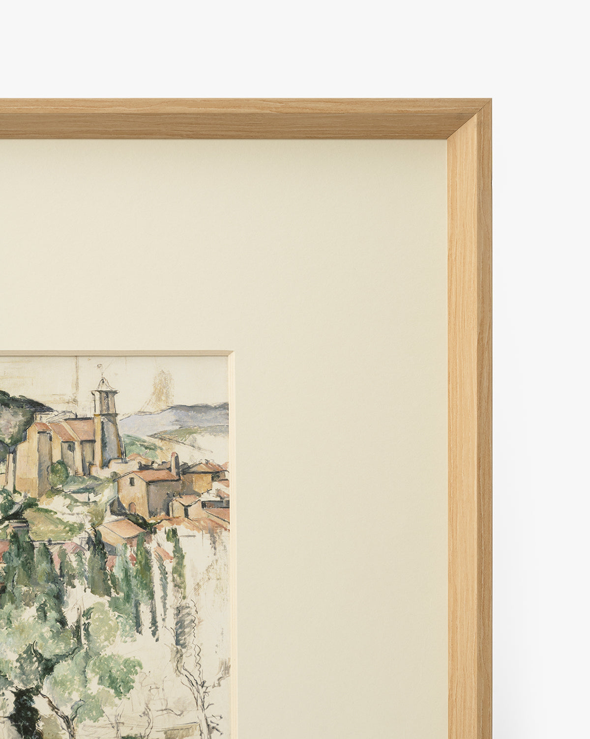 A close-up of Le Village, a museum-quality giclee print, shows part of a hillside village with buildings and greenery, accented by a light mat and an elegant natural woodgrain frame, by Vendixs