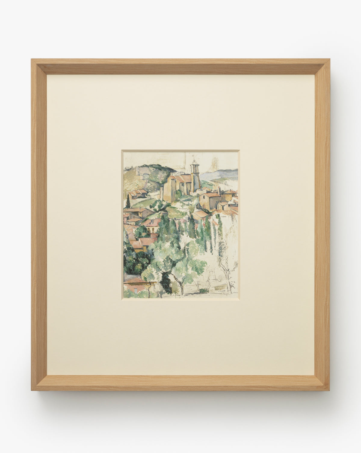 Le Village is a framed watercolor giclee print featuring a hillside town with clustered buildings, church steeple, and soft greenery. Museum-quality, its centered in a wide off-white mat and set in a natural woodgrain frame, by Vendixs
