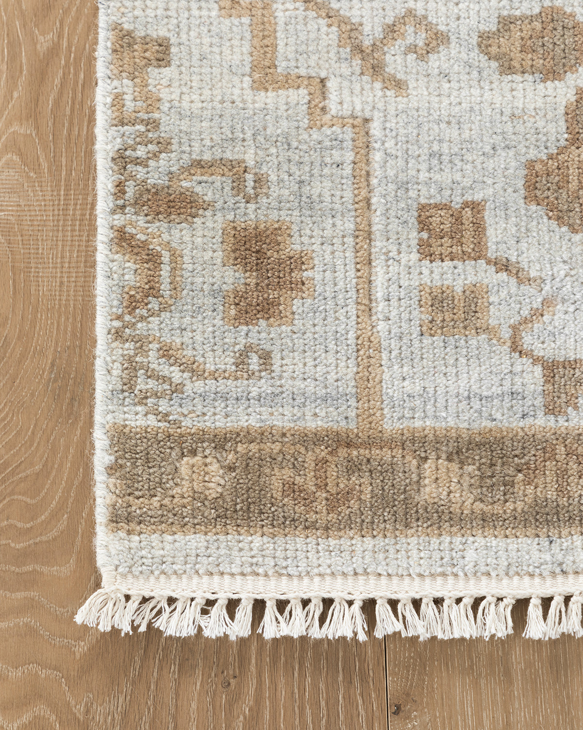 A close-up of the Lexington Hand-Knotted Wool Rug shows its textured wool in beige, brown, and gray tones with fringe edging. This artisan-crafted rug is displayed on a light wood floor, by Vendixs