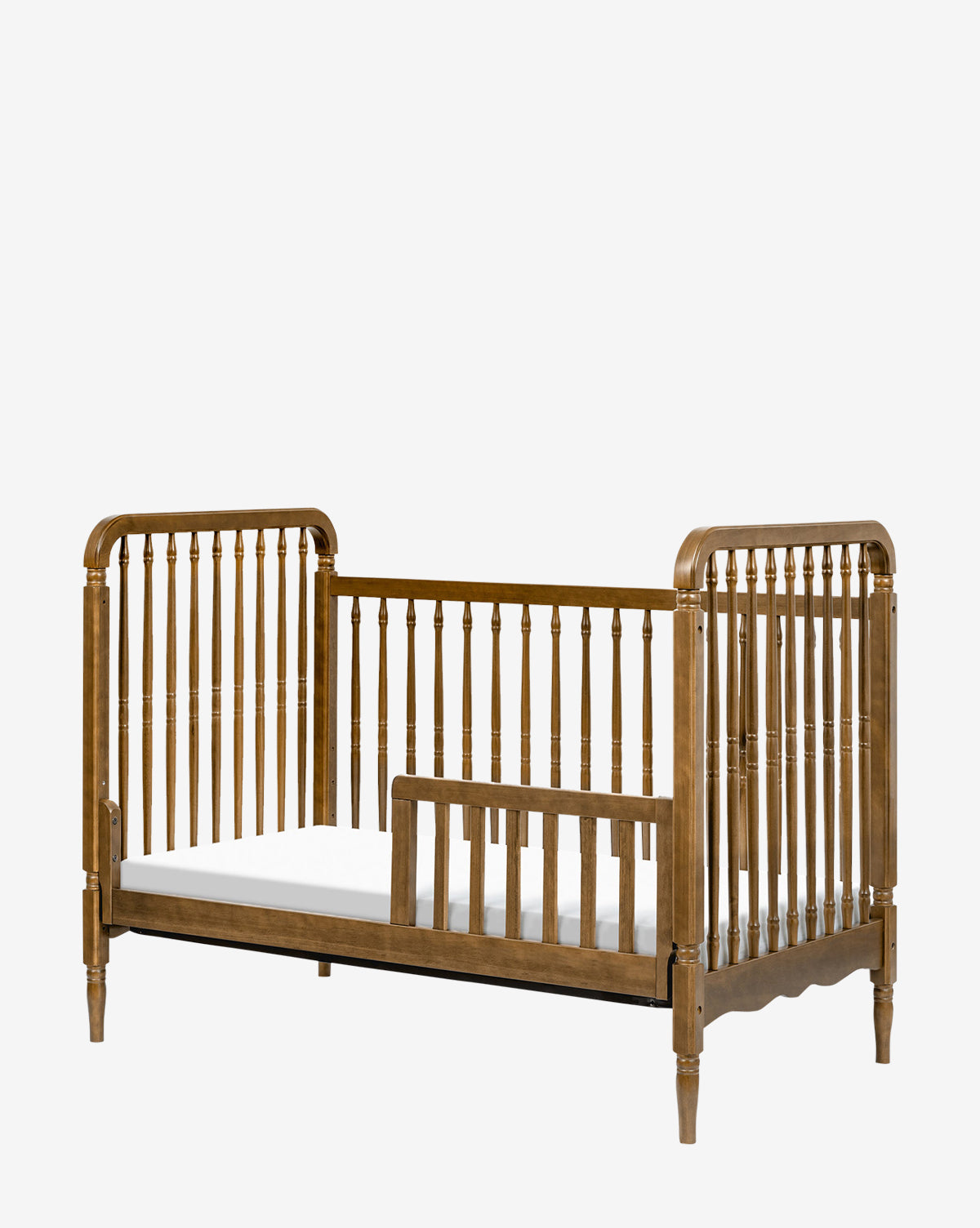 The Liberty 3-in-1 Convertible Spindle Crib with Toddler Bed Conversion Kit features vertical slats, partial safety rail, rounded edges, and decorative posts—shown here as a toddler bed with a white mattress, ideal for your childs transition, by McGee & Co.