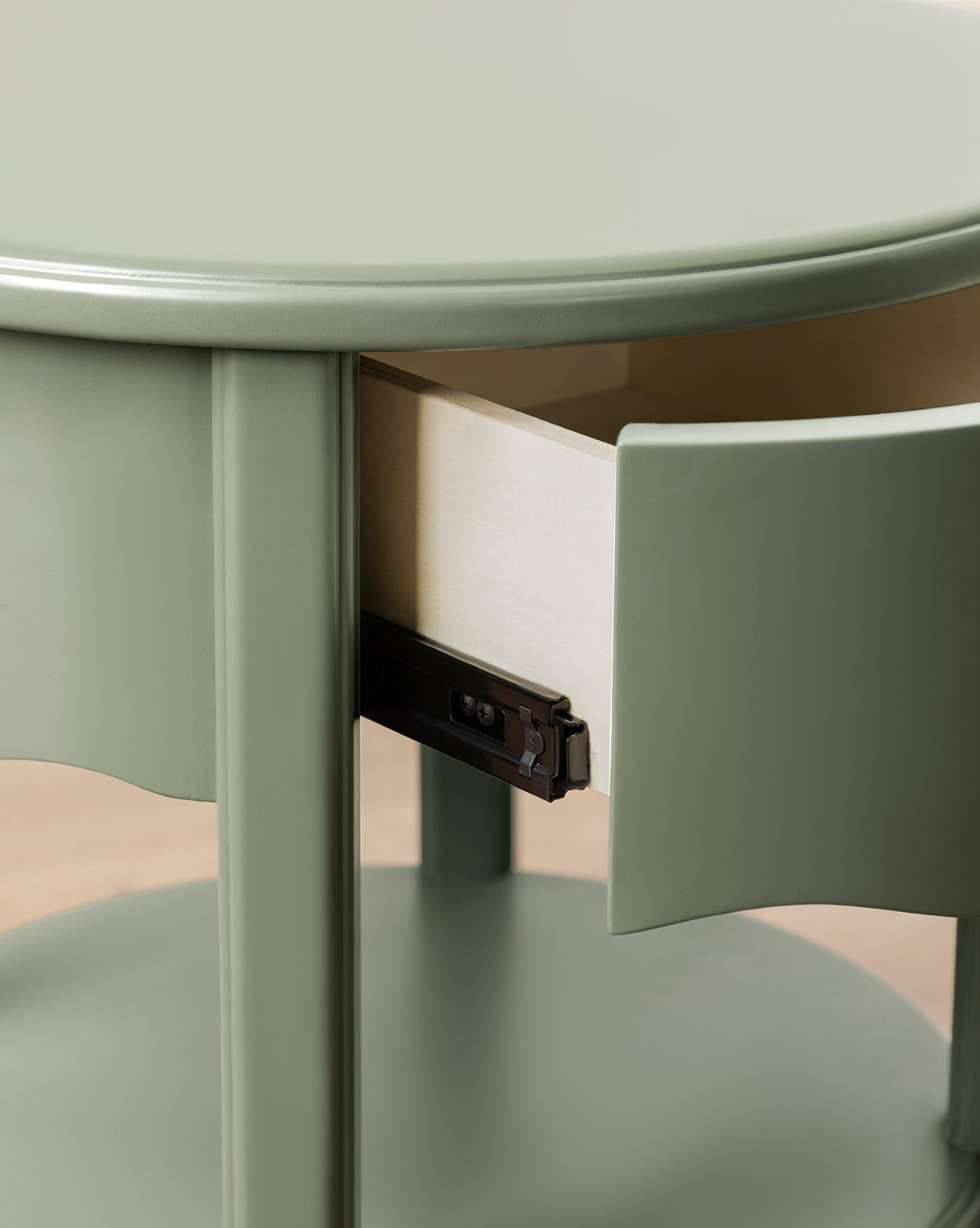 Close-up of the Liberty Nightstand, a round, light green piece with a glossy finish. Its small drawer is partially open, revealing the light wood interior and black metal sliding mechanism, by Vendixs