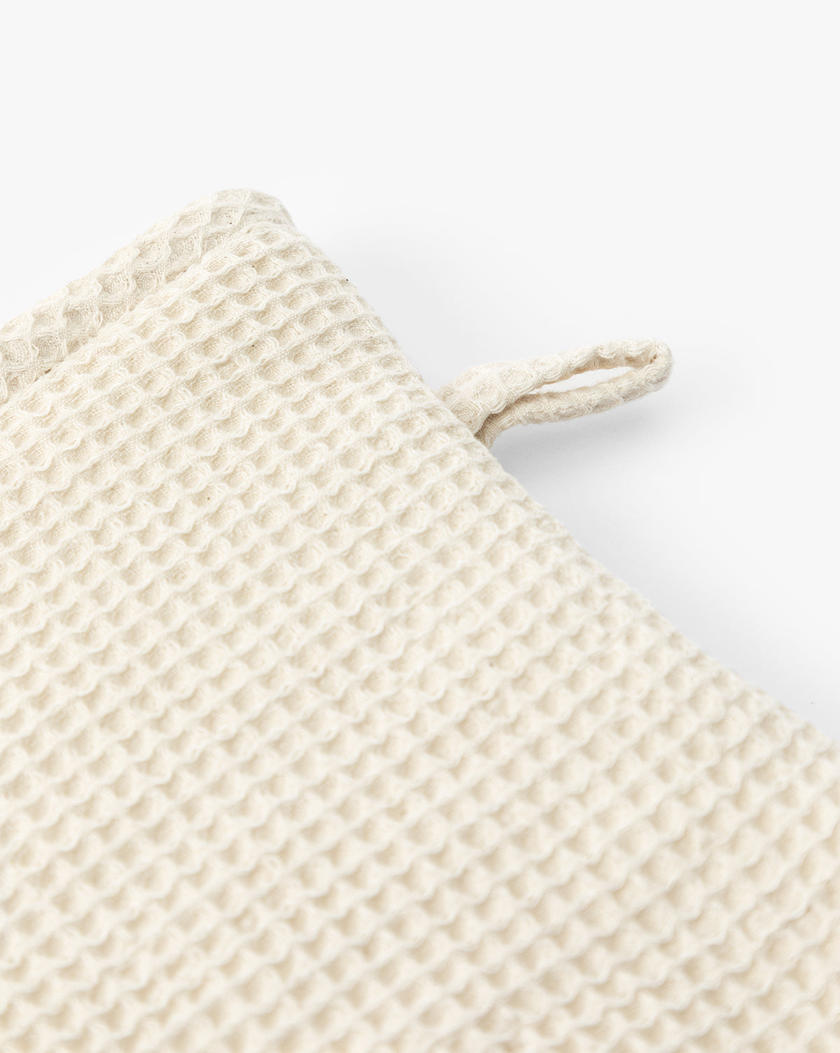 Close-up of a beige, textured waffle-knit fabric with a small loop on the edge—the Linen Blend Waffle Oven Mitt is a kitchen essential, shown against a white background, by Vendixs