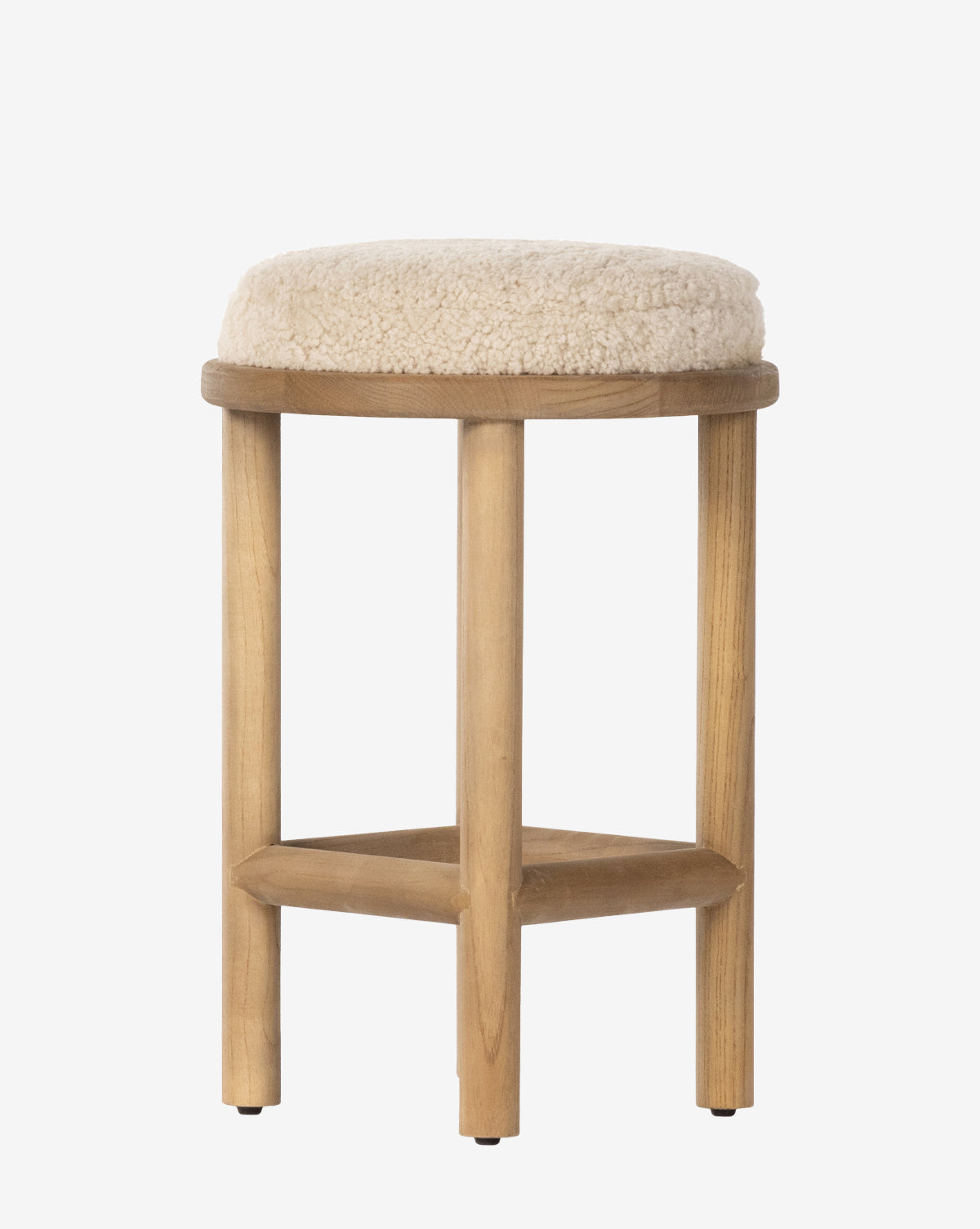 The Linus Stool has four wooden legs and a round, cushioned seat upholstered in soft beige shearling, making it ideal for comfortable counter seating, by McGee & Co.