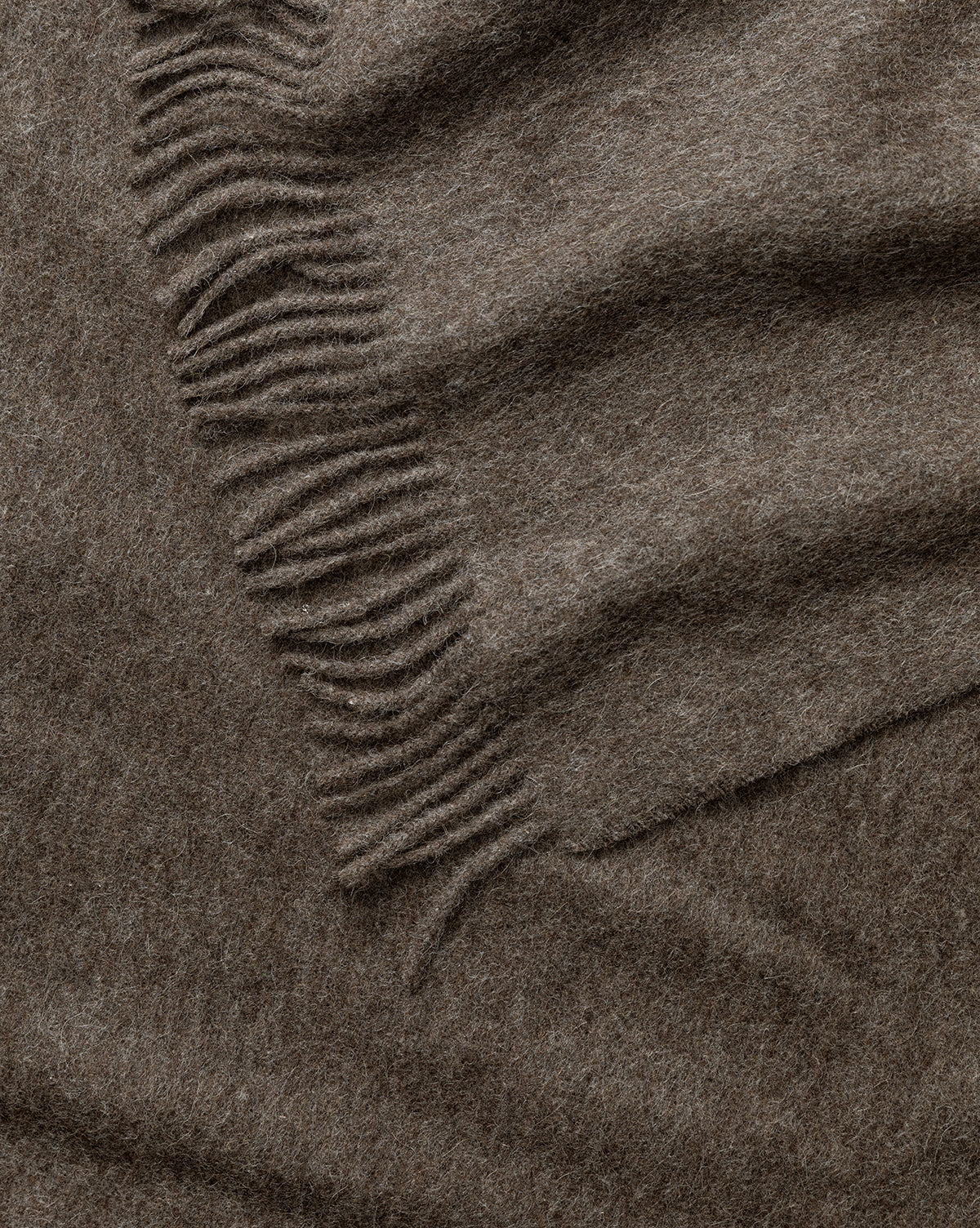 A close-up of the Fibre Locester Throw, crafted from soft brown wool with fringed edges and gentle folds, highlights the cozy, eco-friendly texture of this stylish home accessory by Vendixs