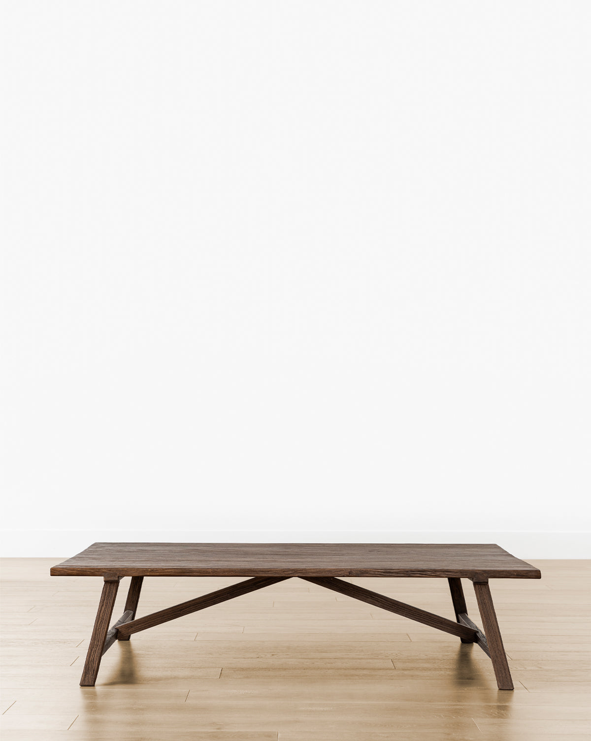 The Lockwood Coffee Table, a low rectangular piece with angled legs in English Oak, sits on a light wood floor against a plain white wall, by Vendixs