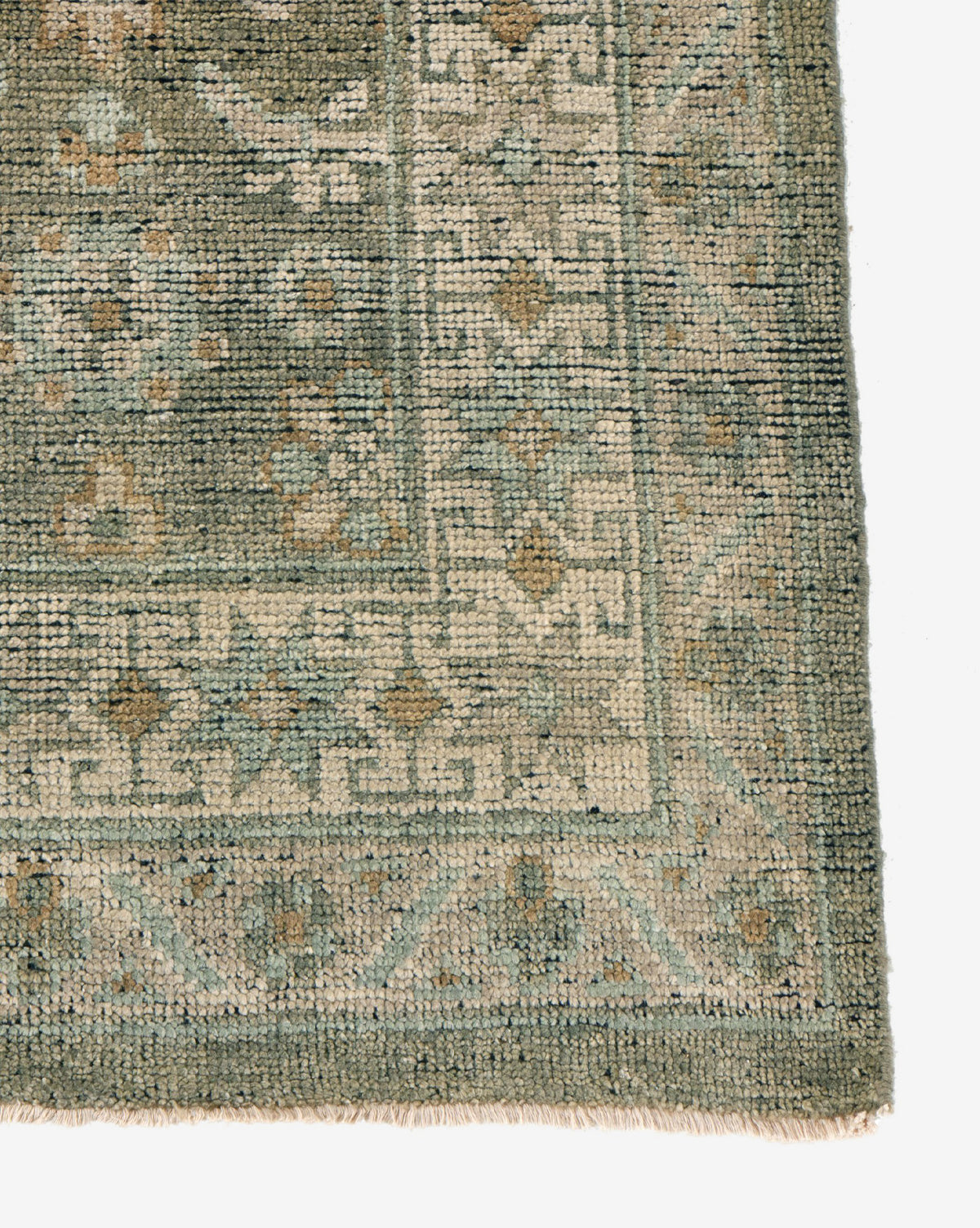 A close-up of the Loreo Hand-Knotted Wool Rug's corner reveals a geometric and floral border in green, beige, and light blue. The visible texture and short fringe showcase the quality craftsmanship of this earth-tone rug, by Vendixs
