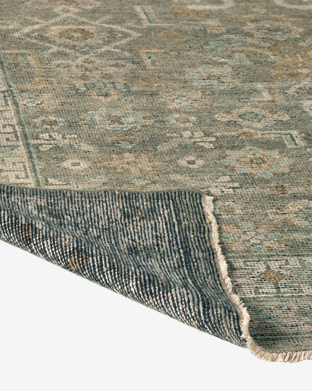 A close-up of the Loreo Hand-Knotted Wool Rug highlights its muted blue and beige geometric pattern, showcasing the detailed texture with a corner folded to reveal the underside, by Vendixs