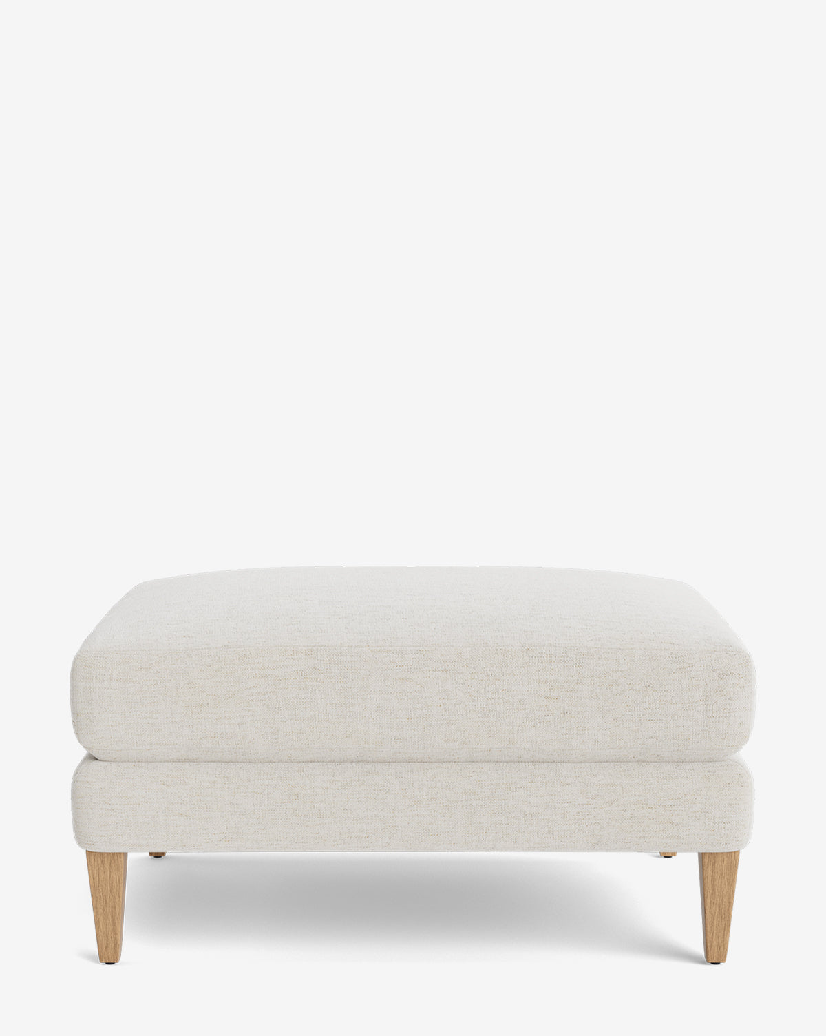 The Lucille Ottoman features a modern rectangular design with light beige upholstery and four angled wooden legs. Shown against a white background, this customizable piece blends style and versatility for any room by Vendixs