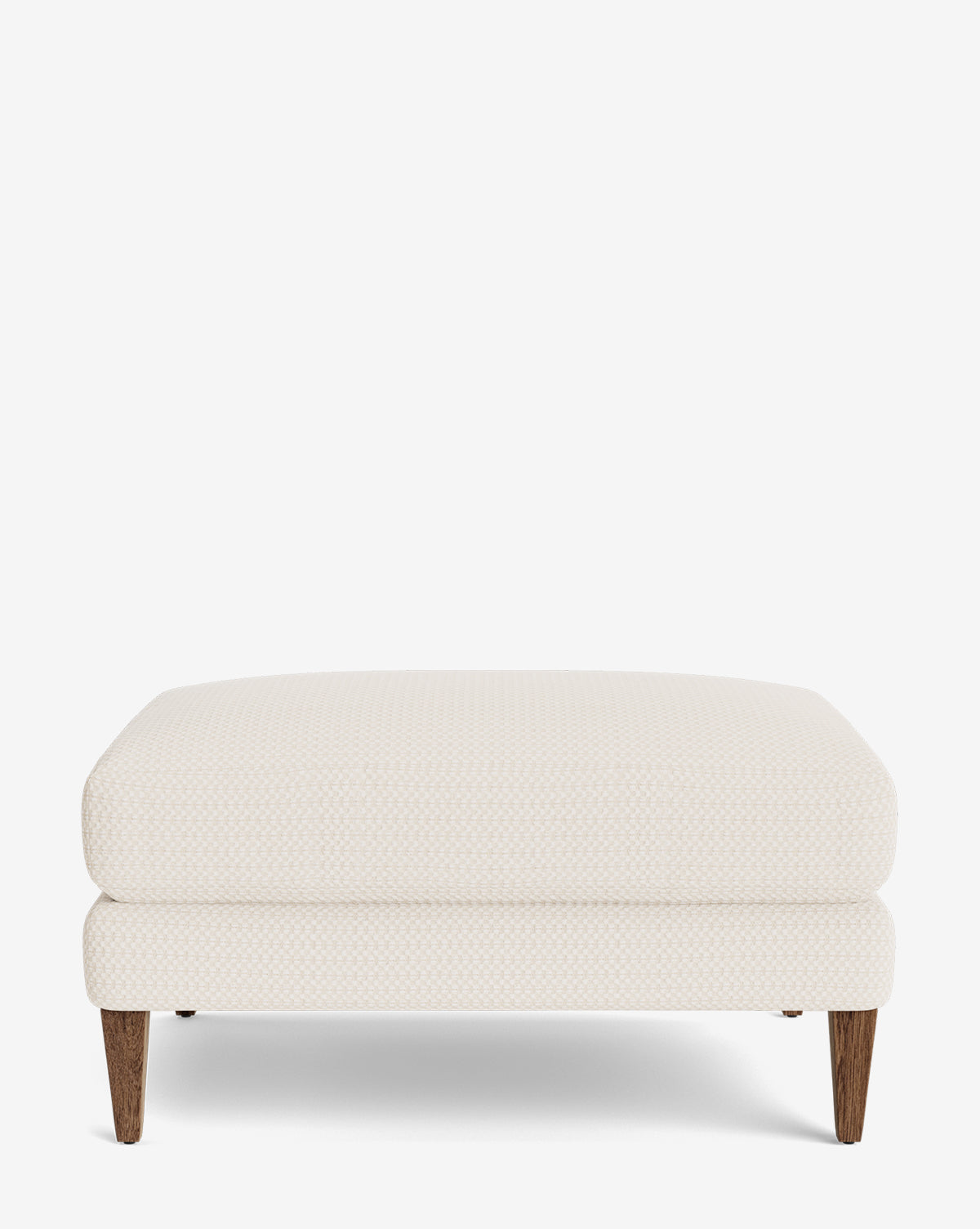 The Lucille Ottoman is a modern, square ottoman in cream with a subtle texture, four sturdy wooden legs, and a minimalist design, shown against a white background by McGee & Co.