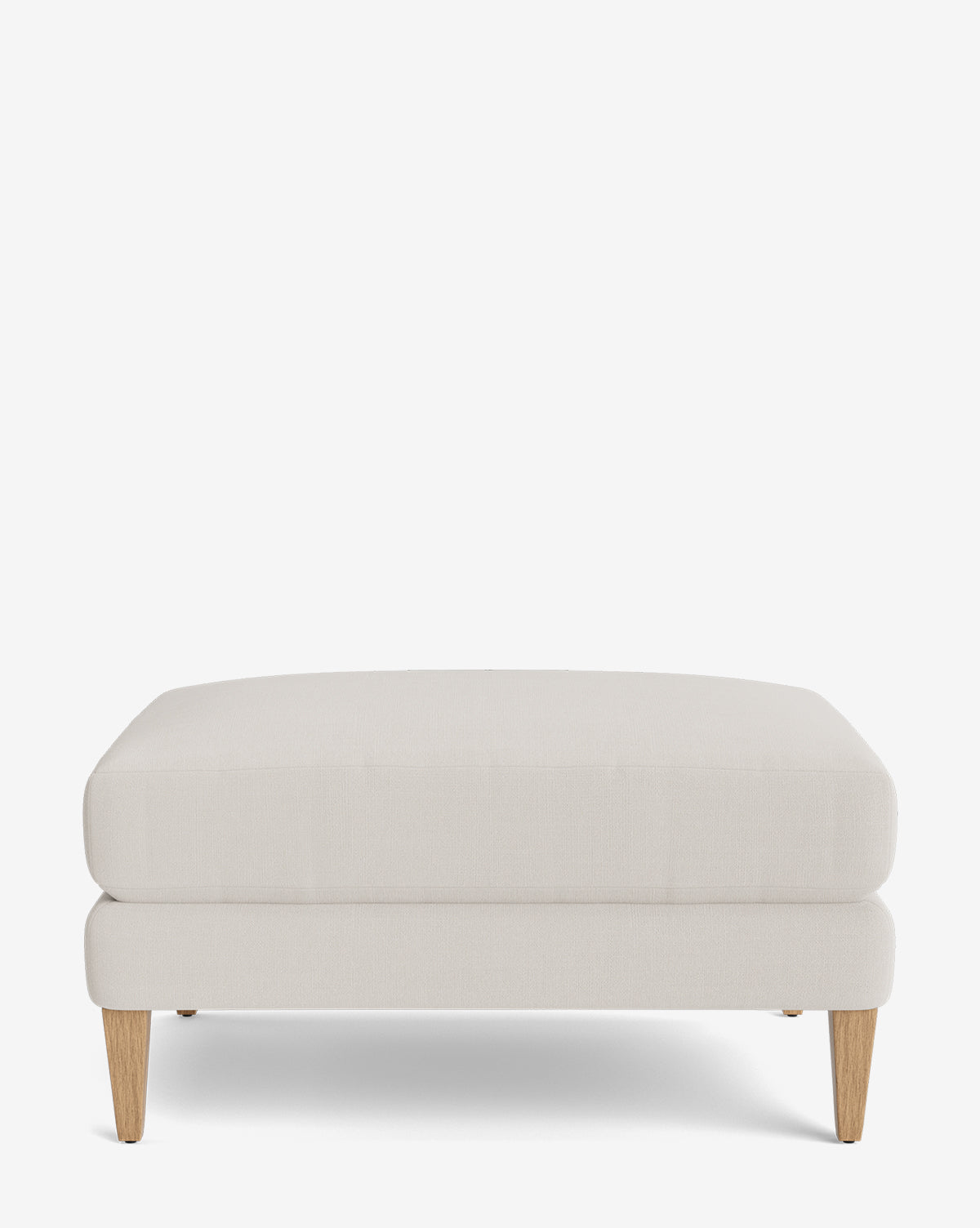 The Lucille Ottoman features a modern design with light beige upholstery and four short, tapered wooden legs, shown against a plain white background by McGee & Co.