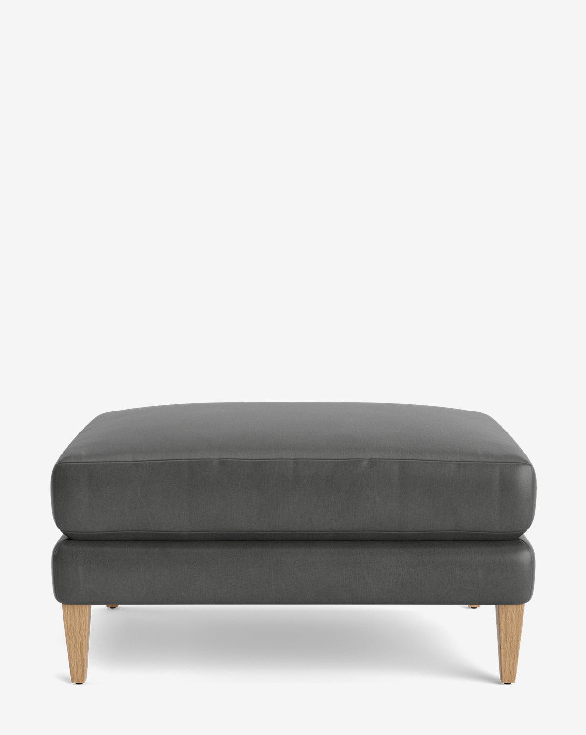The Lucille Ottoman features a modern rectangular design with dark gray upholstery and four light wooden legs, displayed on a plain white background, by McGee & Co.