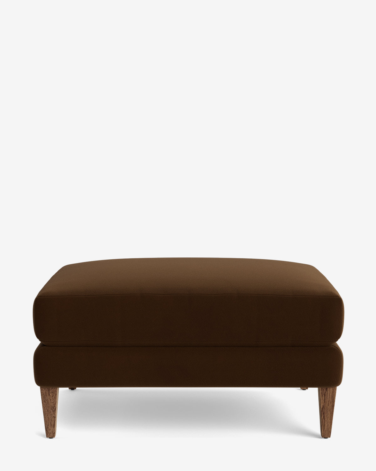 The Lucille Ottoman is a modern rectangular ottoman in dark brown, featuring a cushioned top and four angled wooden legs, displayed on a plain white background by McGee & Co.