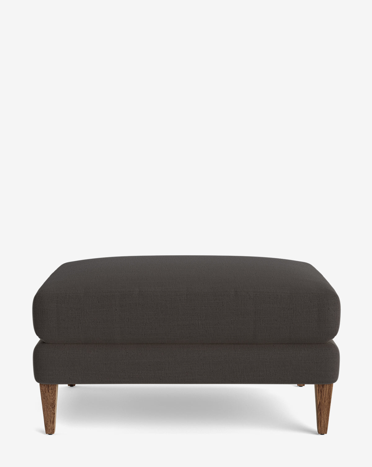 The Lucille Ottoman is a modern rectangular ottoman in dark gray with wooden legs, shown on a plain white background by McGee & Co.