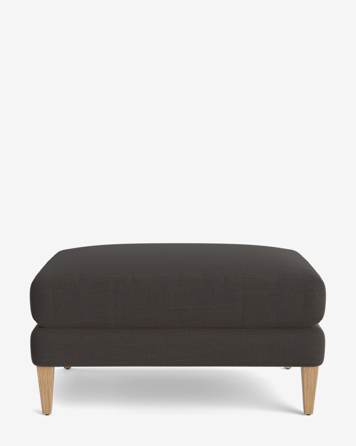 The Lucille Ottoman is a modern rectangular ottoman in dark gray upholstery with light wooden legs, displayed on a plain white background, by McGee & Co.