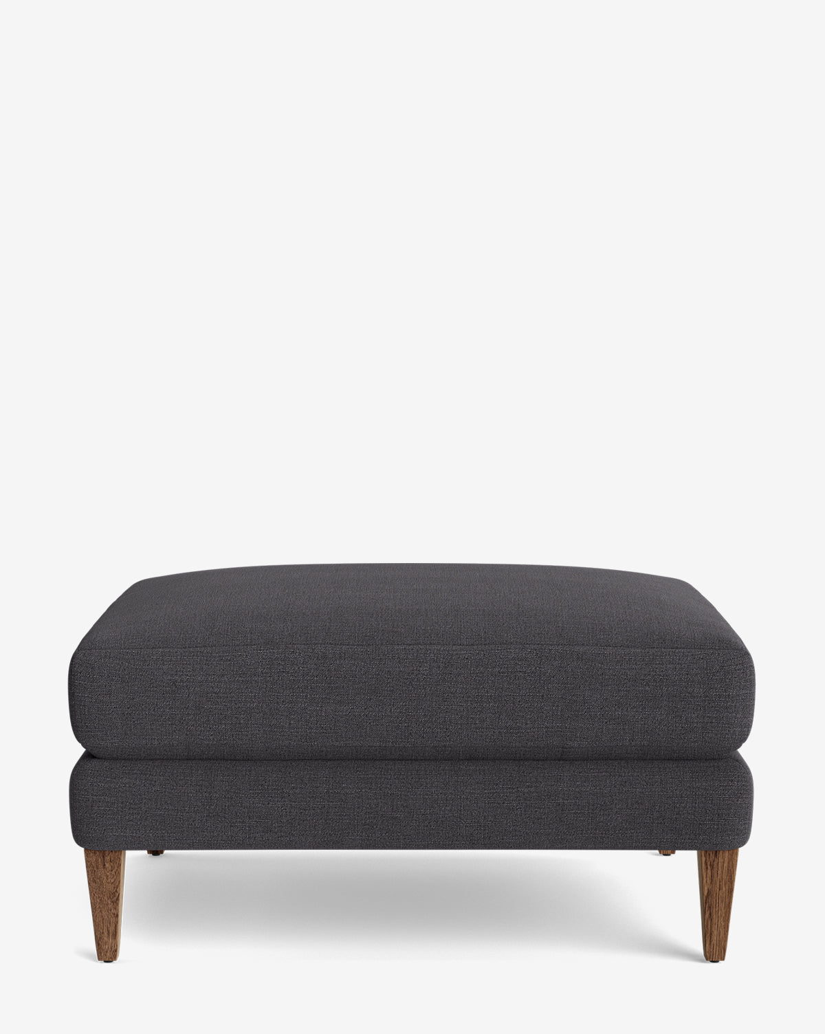 The Lucille Ottoman features a rectangular shape in dark gray with short wooden legs, shown against a plain white background—a modern piece ideal for stylish, customizable living spaces by McGee & Co.