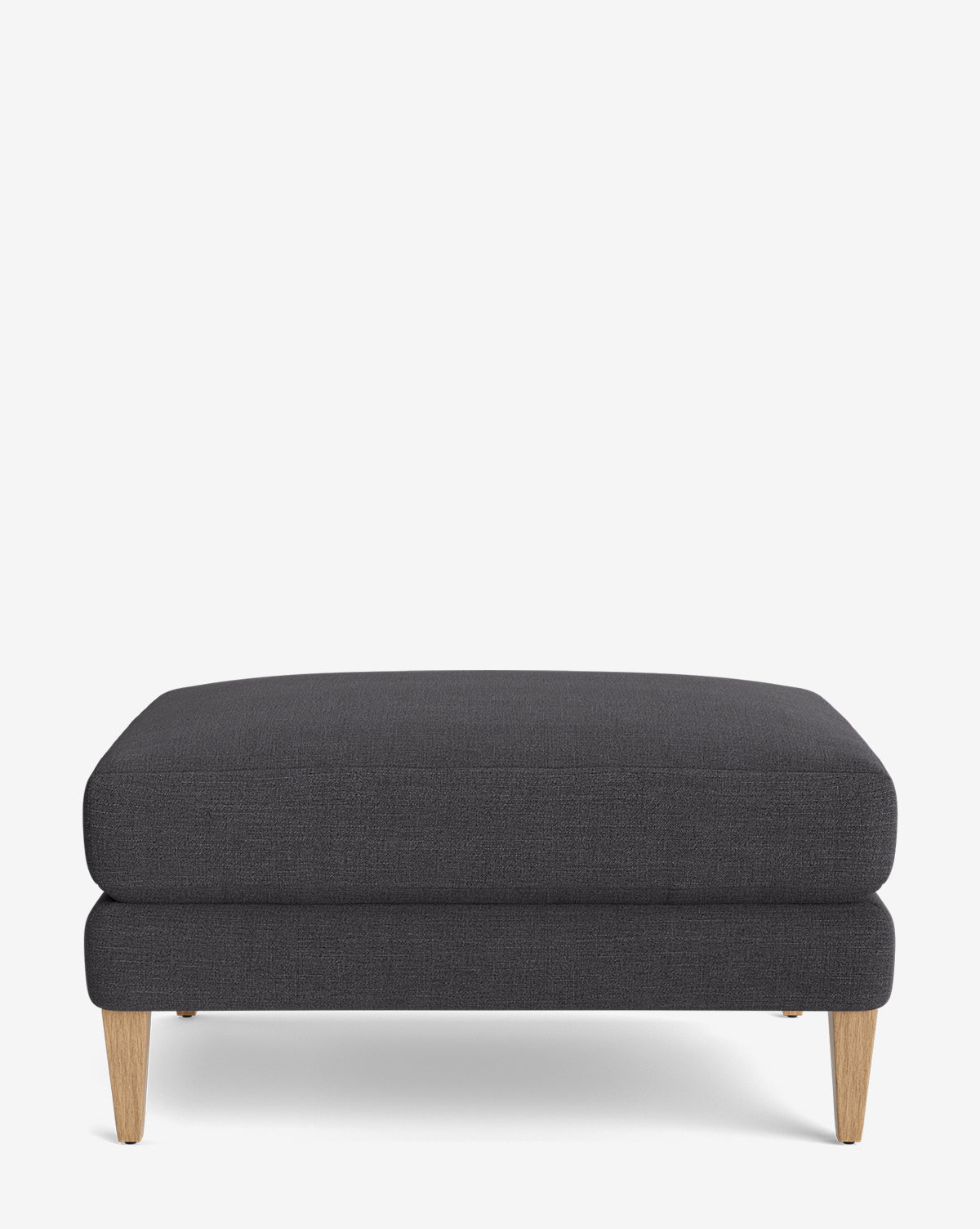 The Lucille Ottoman is a modern, rectangular ottoman with dark gray upholstery and wooden legs, displayed on a plain white background, by McGee & Co.