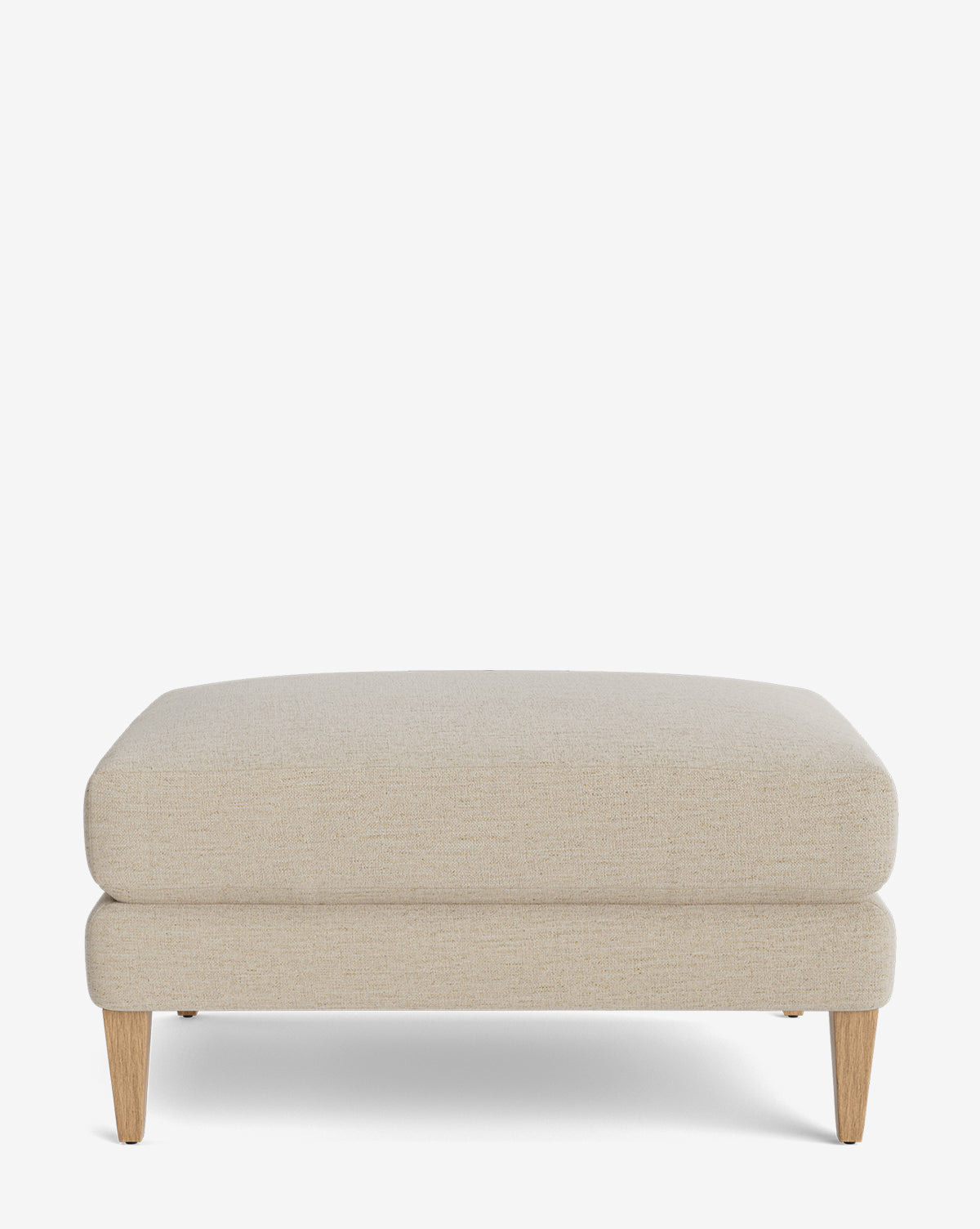 The Lucille Ottoman showcases modern style with its beige upholstery, cushioned top, and four angled wooden legs, displayed on a plain white background by McGee & Co.
