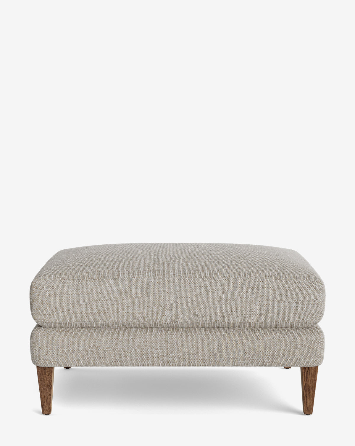 The Lucille Ottoman is a modern, rectangular piece with light gray upholstery, a cushioned top, and four tapered wooden legs, by McGee & Co. It’s displayed against a plain white background.