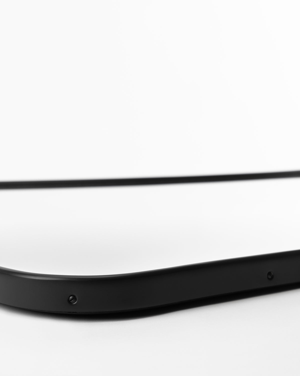 A close-up of the corner of the rectangular Ludwig Wall Mirror with a black frame, set against a white background, highlighting its smooth edge and visible screws, by Vendixs