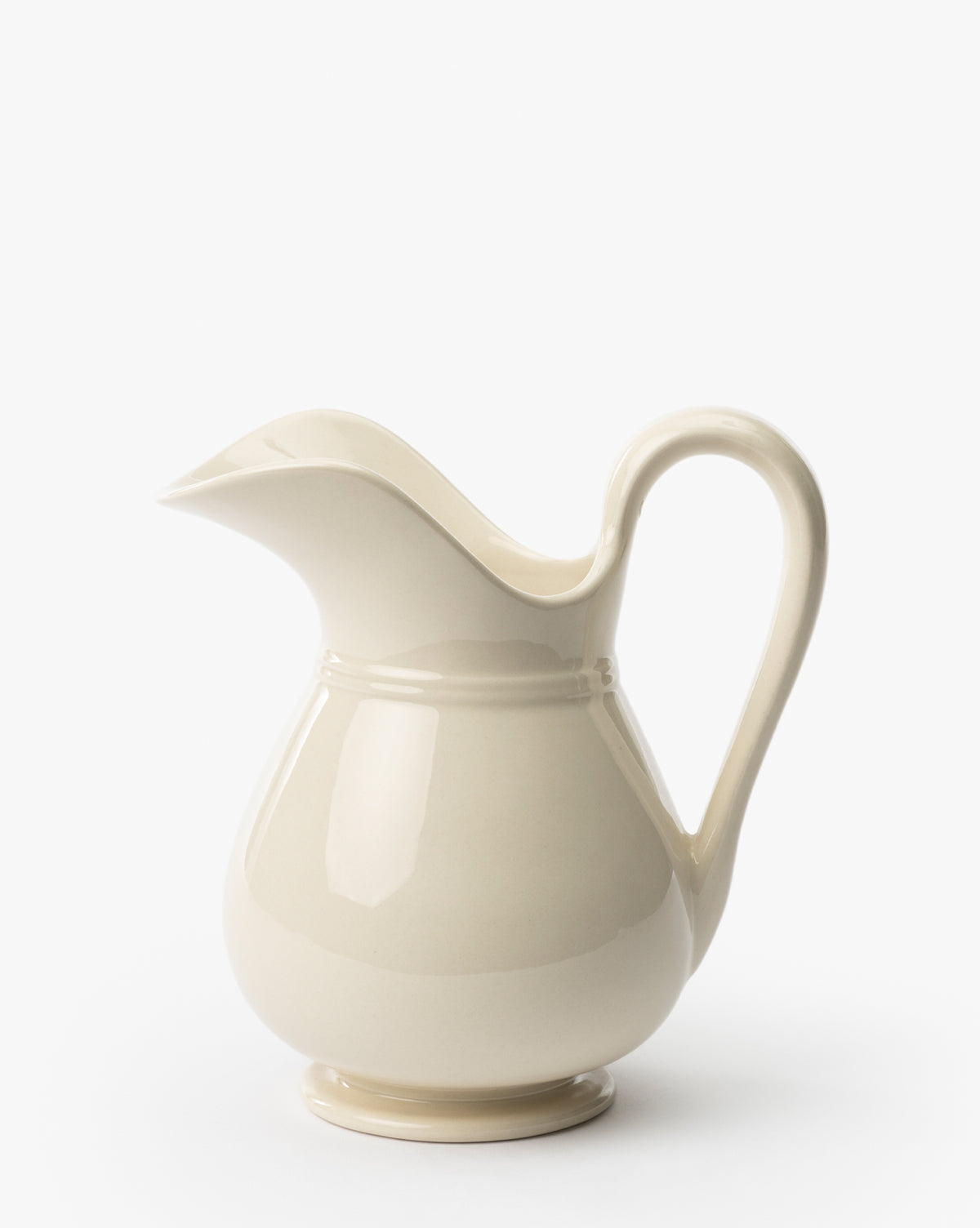 The Lumen Pitcher is a cream-colored stoneware piece with a curved handle, wide spout, and smooth white finish, shown on a plain white background, by Vendixs