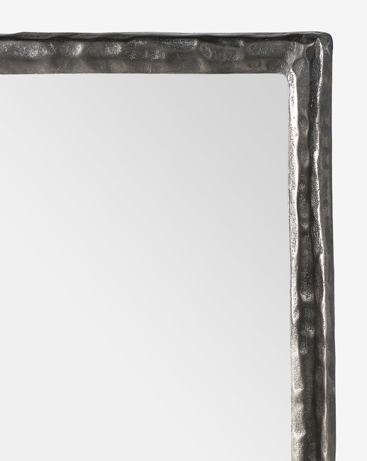 A close-up of the top right corner of the Lumi Wall Mirror, showcasing its textured, metallic hammered frame. The mirror’s surface is smooth and softly reflects light, by McGee & Co.