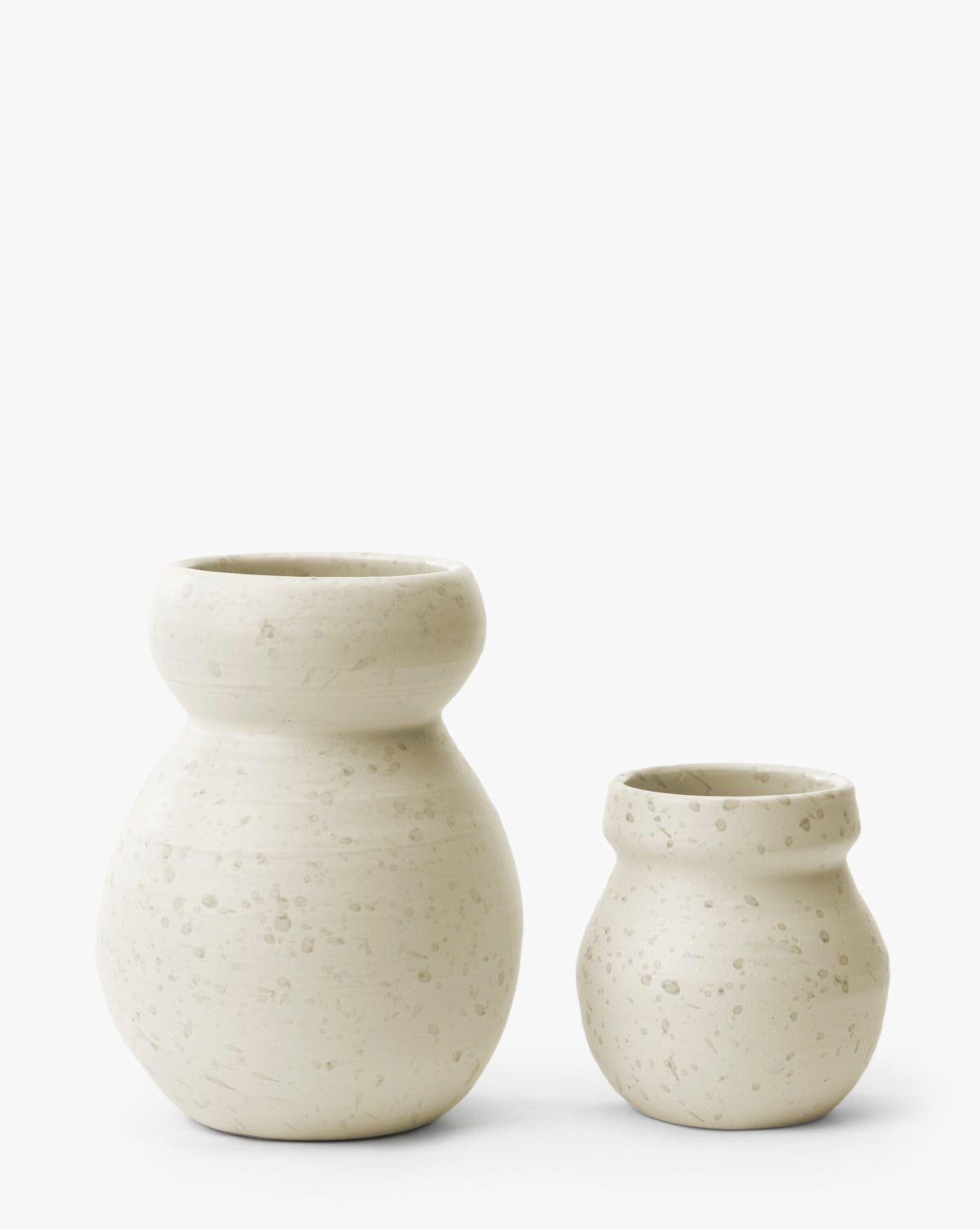 Two off-white Lyra Vases with wide necks and a subtle speckled texture are placed side by side on a plain white background. The larger white ceramic vase is on the left, and the smaller one is on the right, by Vendixs
