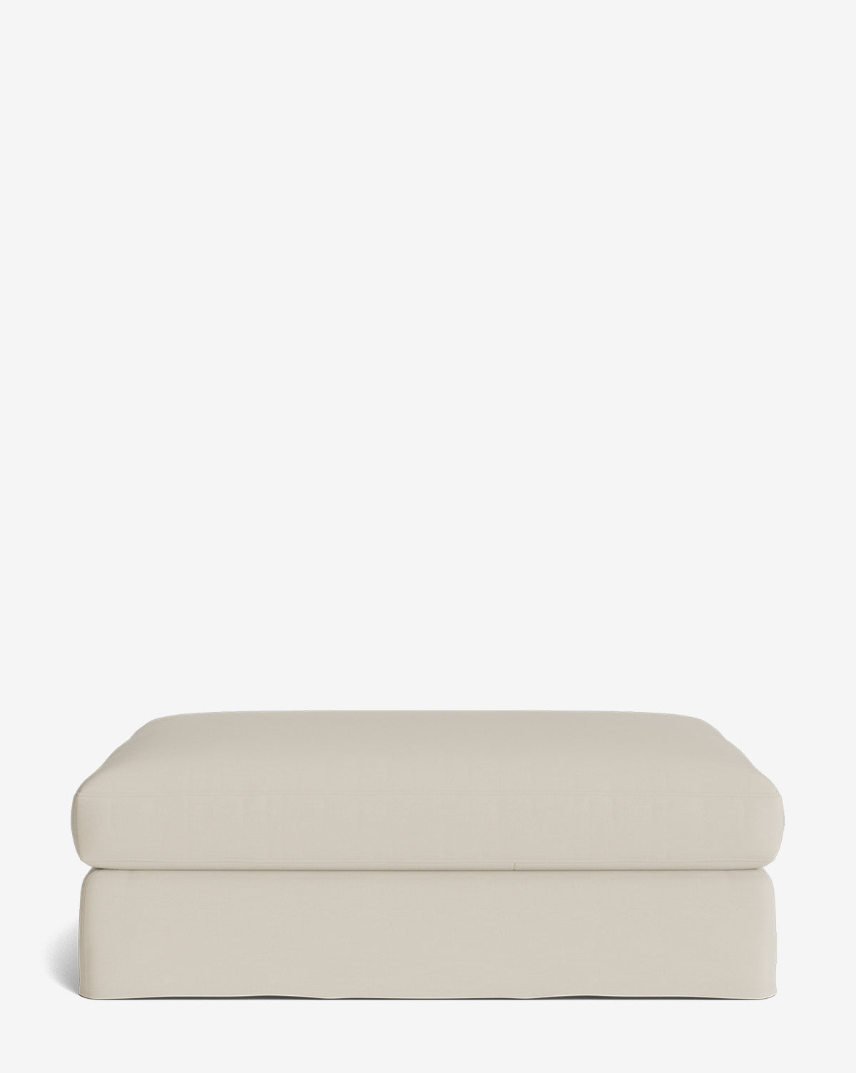 The Macy Slipcover Ottoman is a rectangular, light beige upholstered piece with soft, rounded edges, ideal for versatile living room use, displayed against a plain white background by McGee & Co.