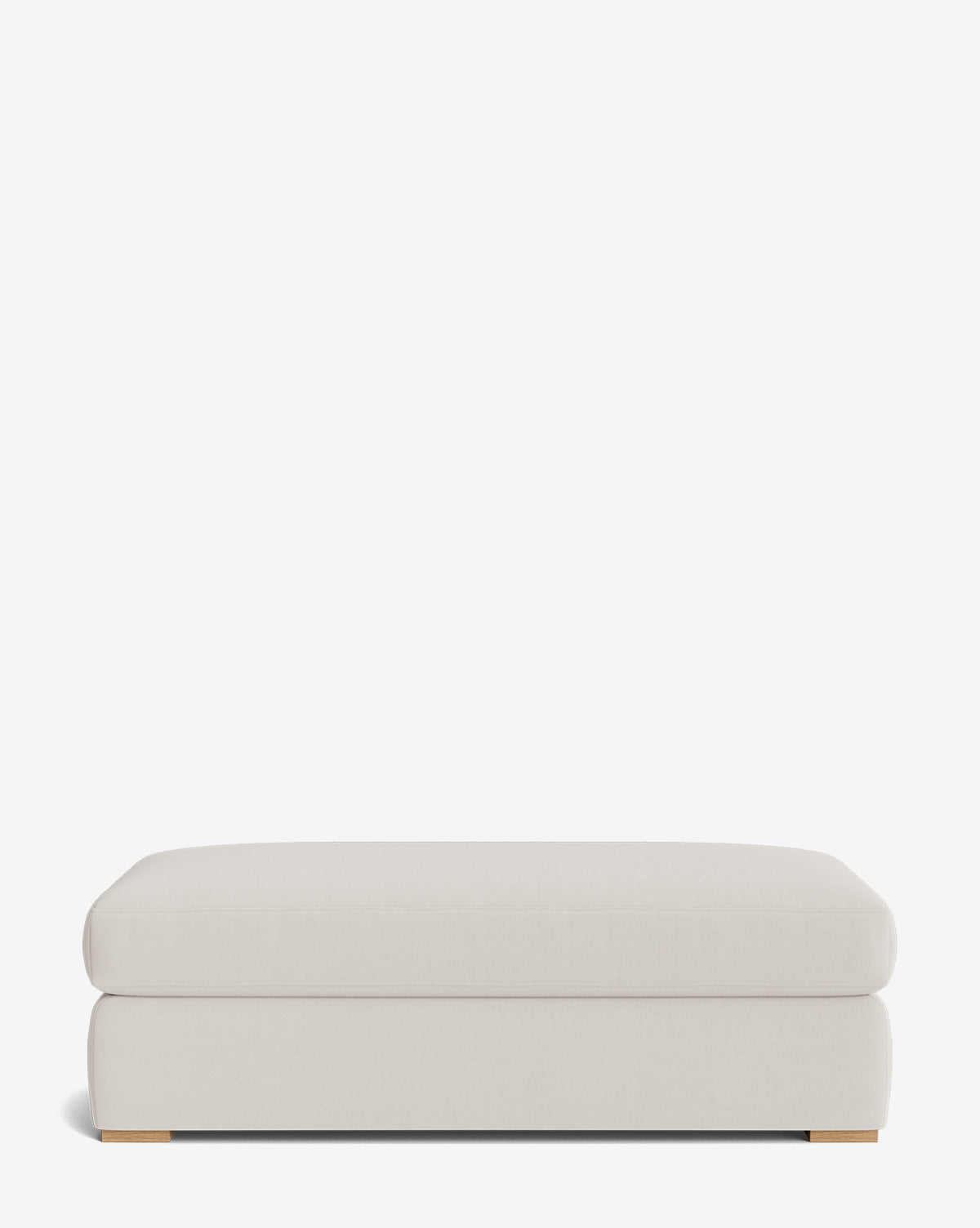 The Macy Upholstered Ottoman is a large, rectangular light beige piece with soft, rounded edges and low wooden feet, ideal for living room decor, by Vendixs Shown against a plain white background.