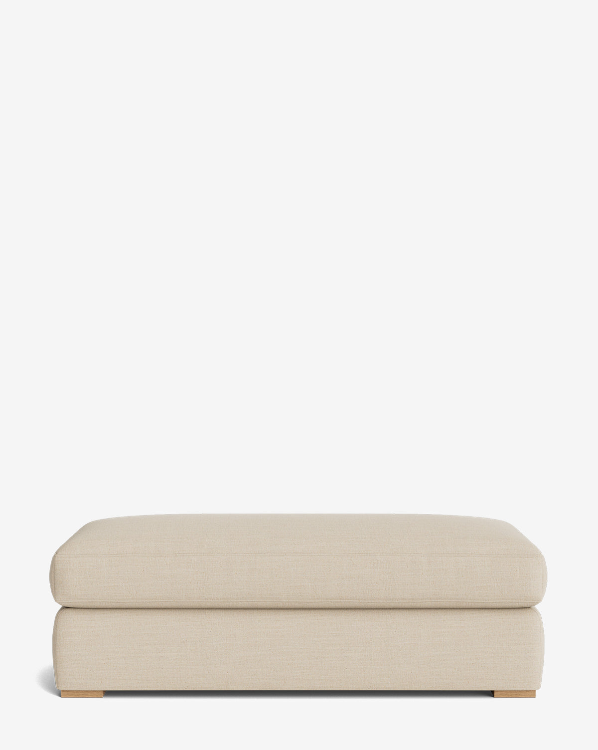 The Macy Upholstered Ottoman is a large, rectangular piece with a soft, cushioned top and low wooden feet, ideal for living room furniture, by McGee & Co. Shown here against a plain white background.