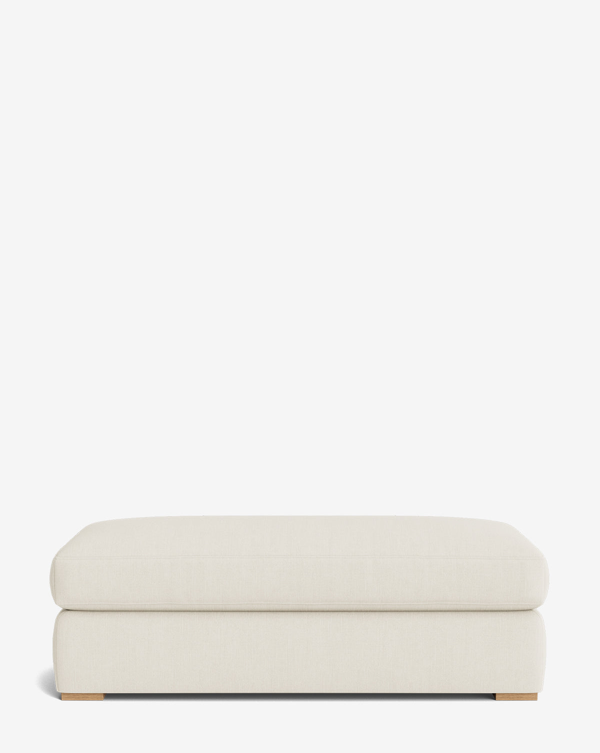 The Macy Upholstered Ottoman is a rectangular, cream-colored piece with a plush cushion and low wooden feet, ideal as customizable living room furniture, shown against a plain white background by McGee & Co.