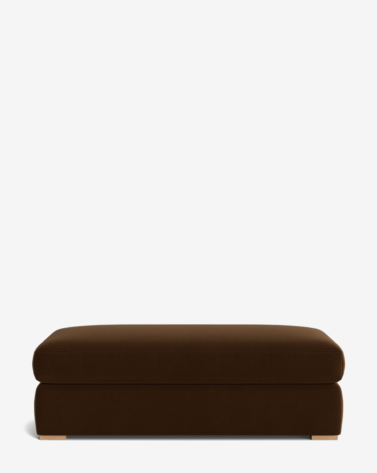 The Macy Upholstered Ottoman is a rectangular, dark brown piece with a smooth surface and low-profile design. It features short, light-colored feet and is displayed against a plain white background, by McGee & Co.