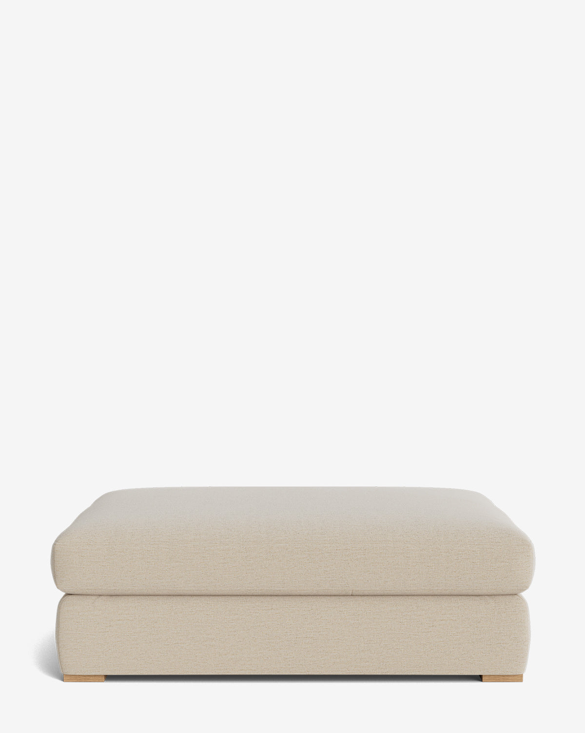 The Macy Upholstered Ottoman is a rectangular beige piece with soft, rounded edges, a flat top, and short wooden legs. Customizable and versatile, it’s ideal for living rooms and shown here against a plain white background by McGee & Co.